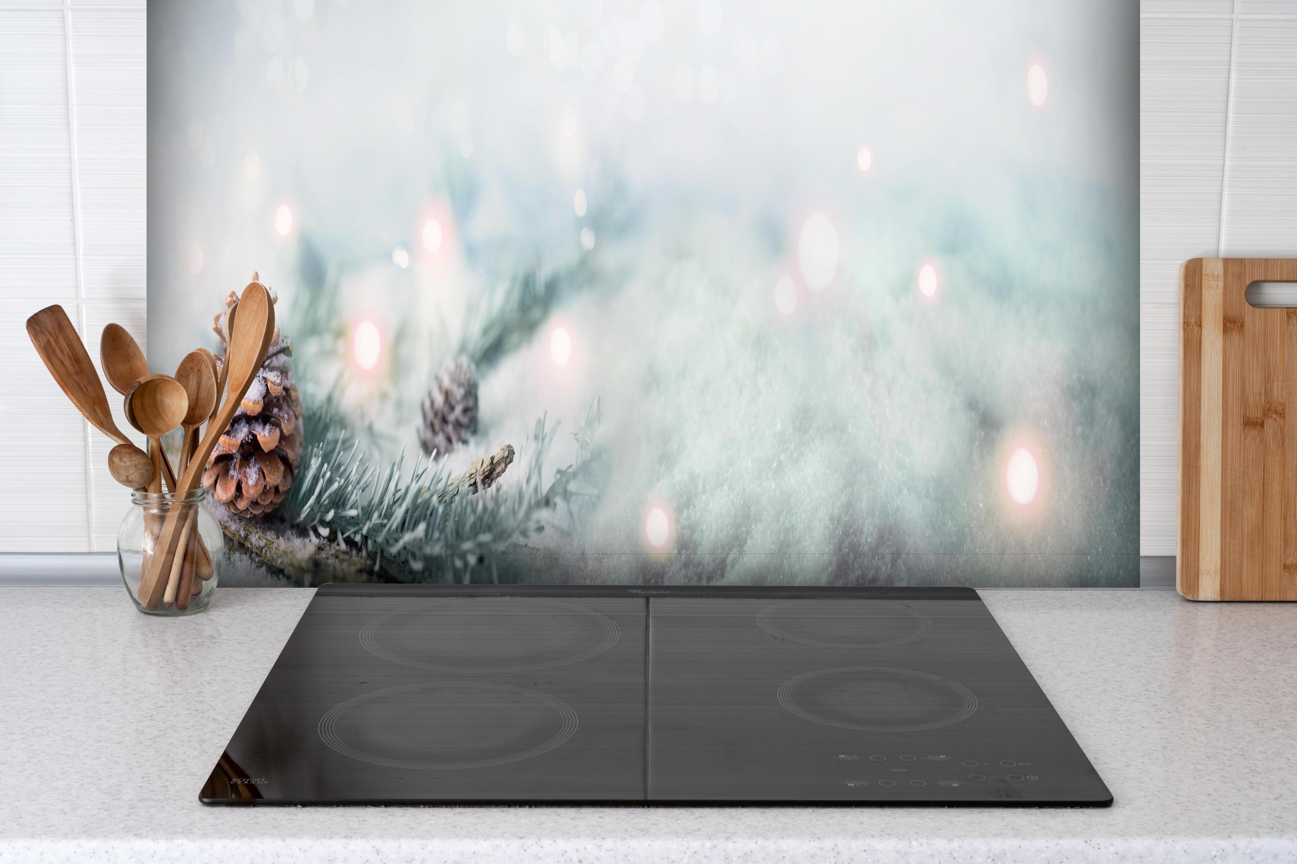 Spritzschutz - Magische Winterlandschaft in Weiß und Grau hinter einem Cerankochfeld zwischen Holz-Kochutensilien