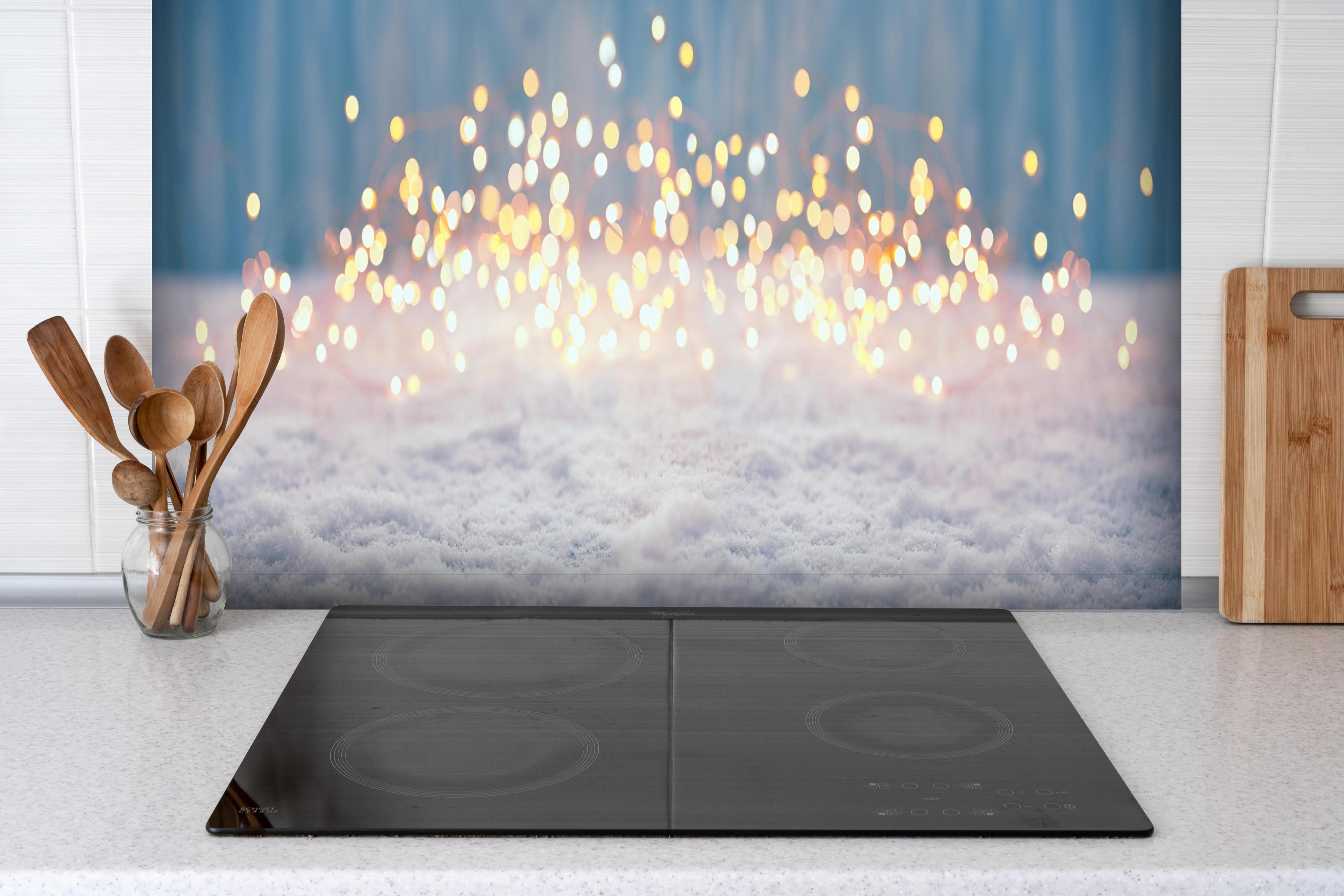 Spritzschutz - Magische Winterlandschaft mit goldenem Bokeh hinter einem Cerankochfeld zwischen Holz-Kochutensilien