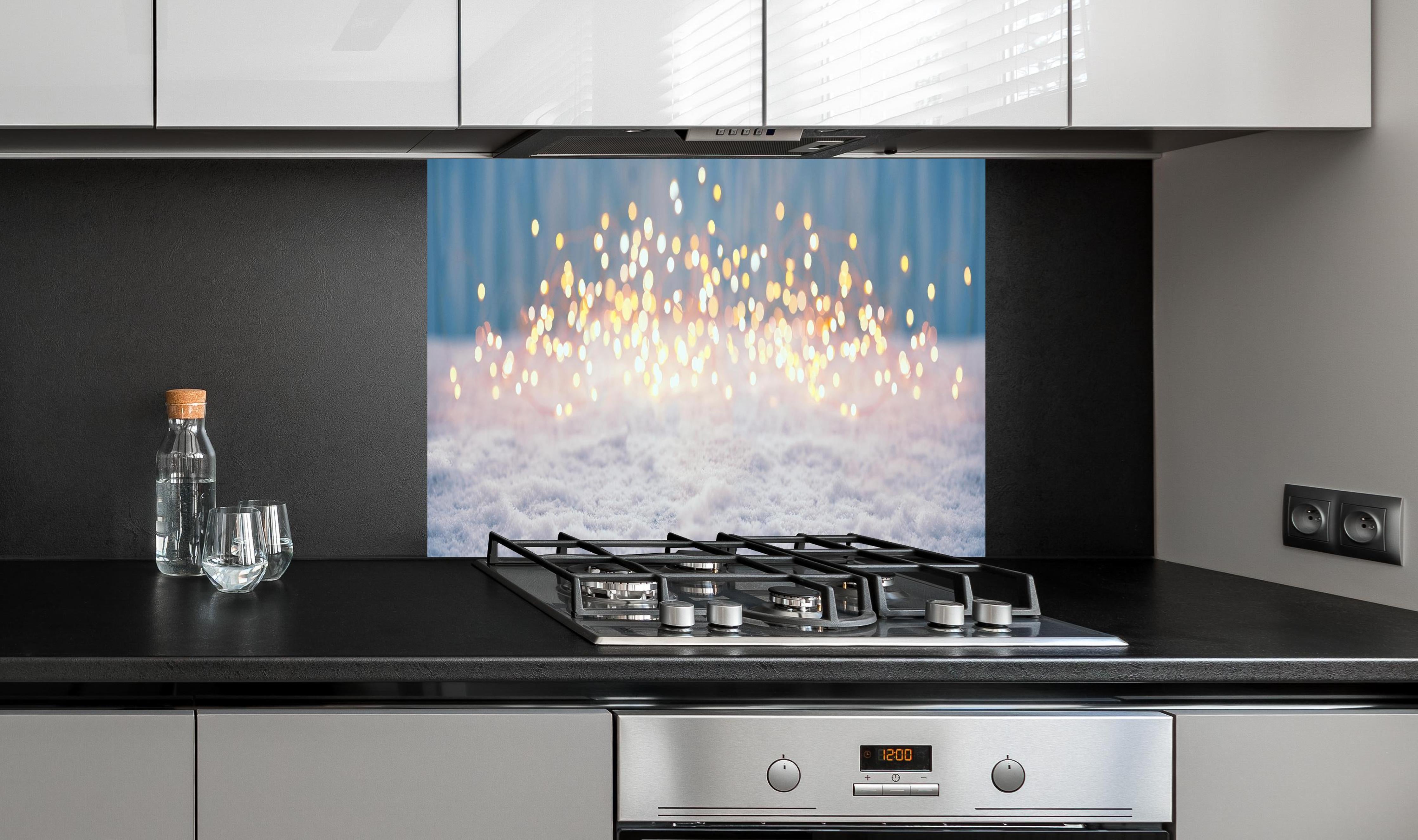 Spritzschutz - Magische Winterlandschaft mit goldenem Bokeh hinter einem Cerankochfeld zwischen Holz-Kochutensilien