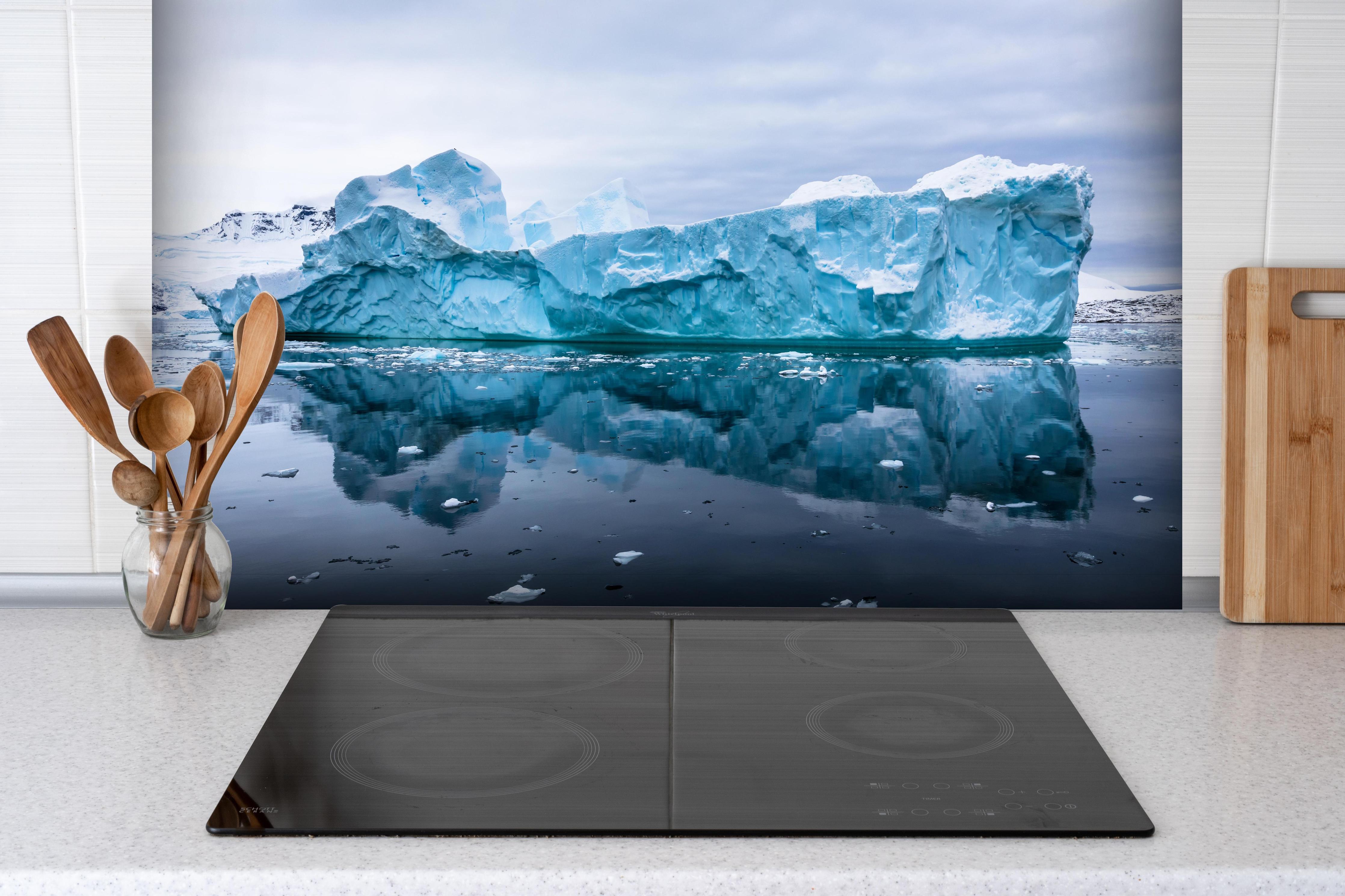 Spritzschutz - Majestätischer Antarktis Eisberg mit Reflexion hinter einem Cerankochfeld zwischen Holz-Kochutensilien