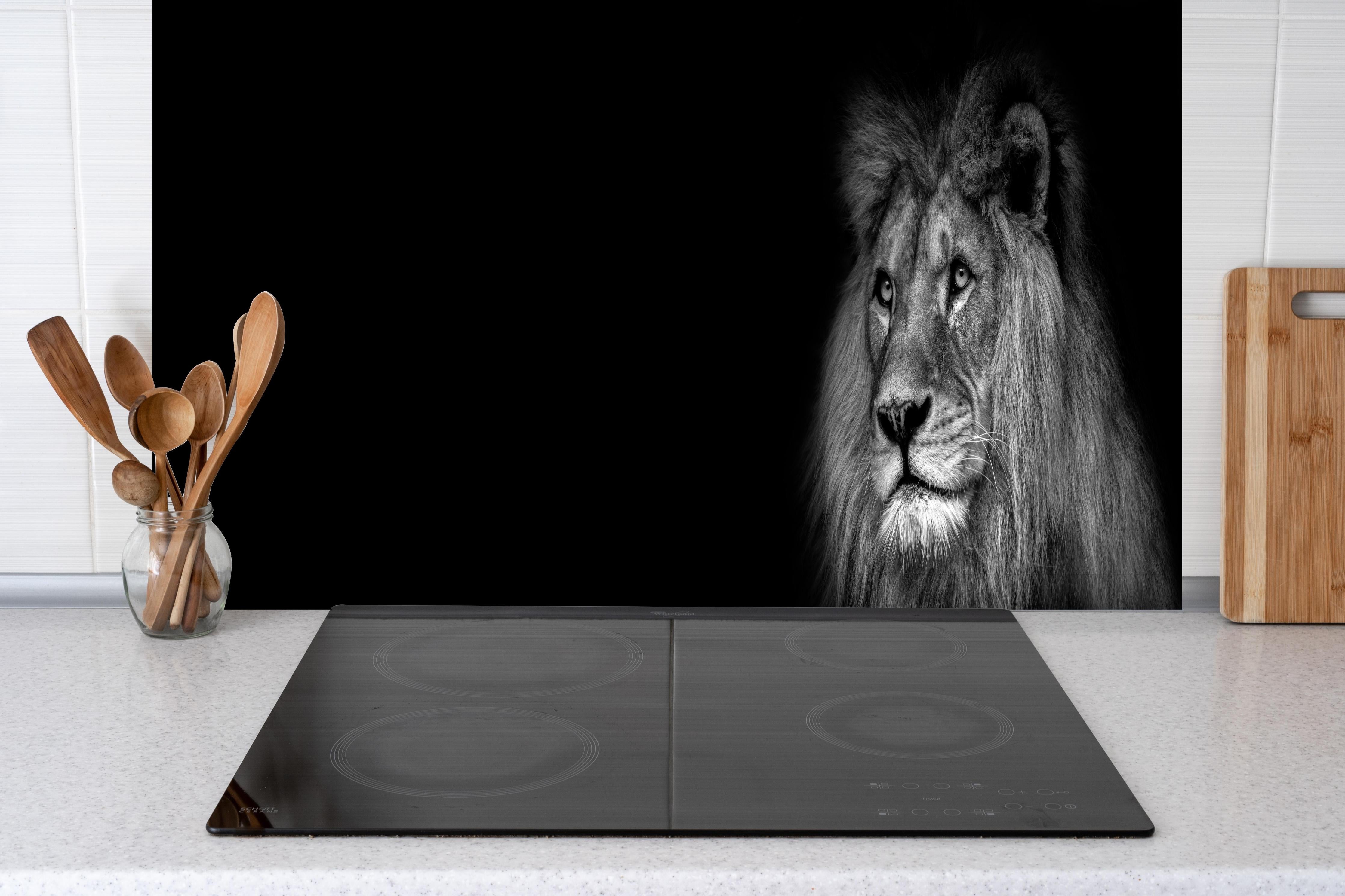 Spritzschutz - Markantes Löwen Gesicht Schwarz-Weiß hinter einem Cerankochfeld zwischen Holz-Kochutensilien