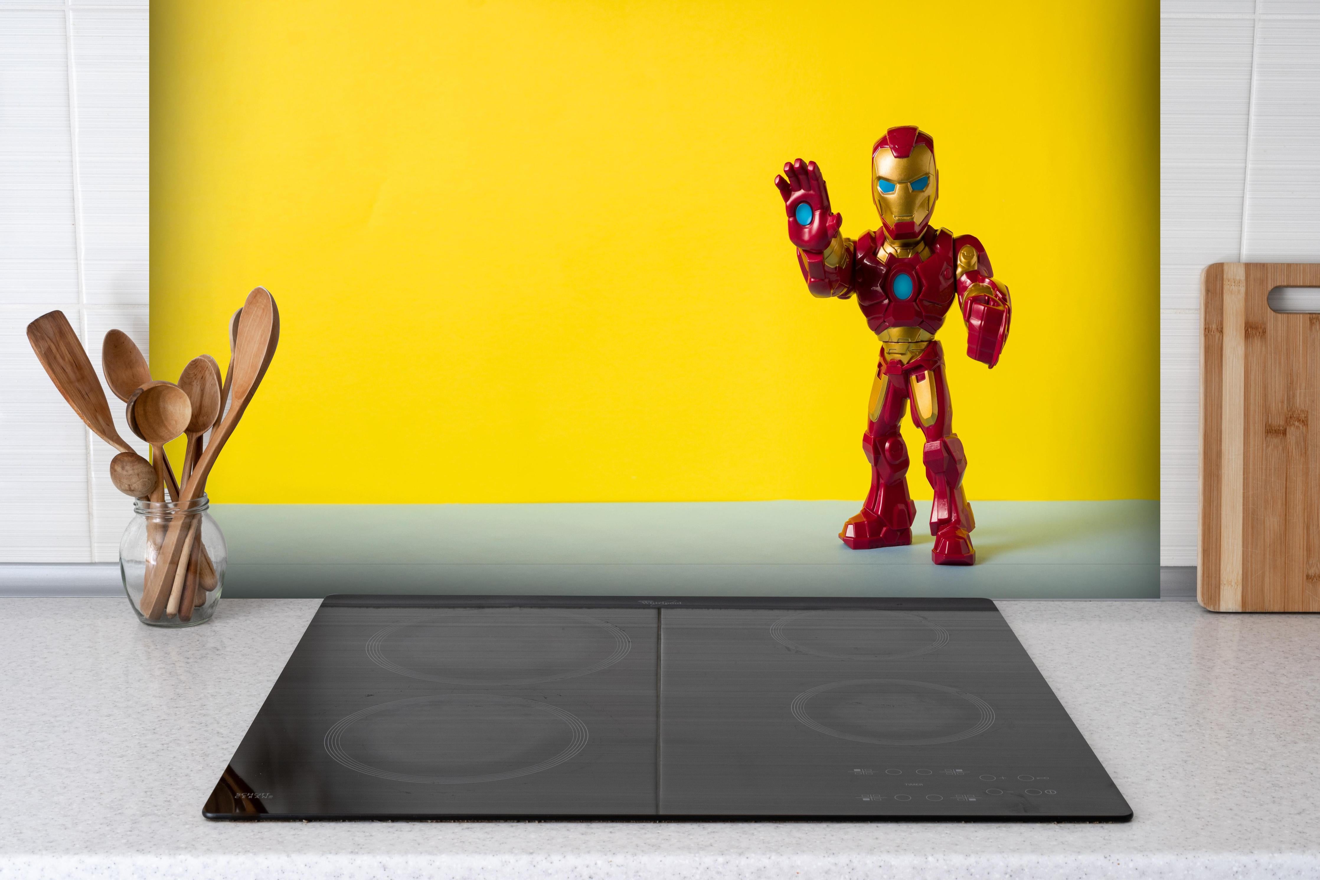 Spritzschutz - Marvel Iron Man Sammelfigur auf Gelb hinter einem Cerankochfeld zwischen Holz-Kochutensilien
