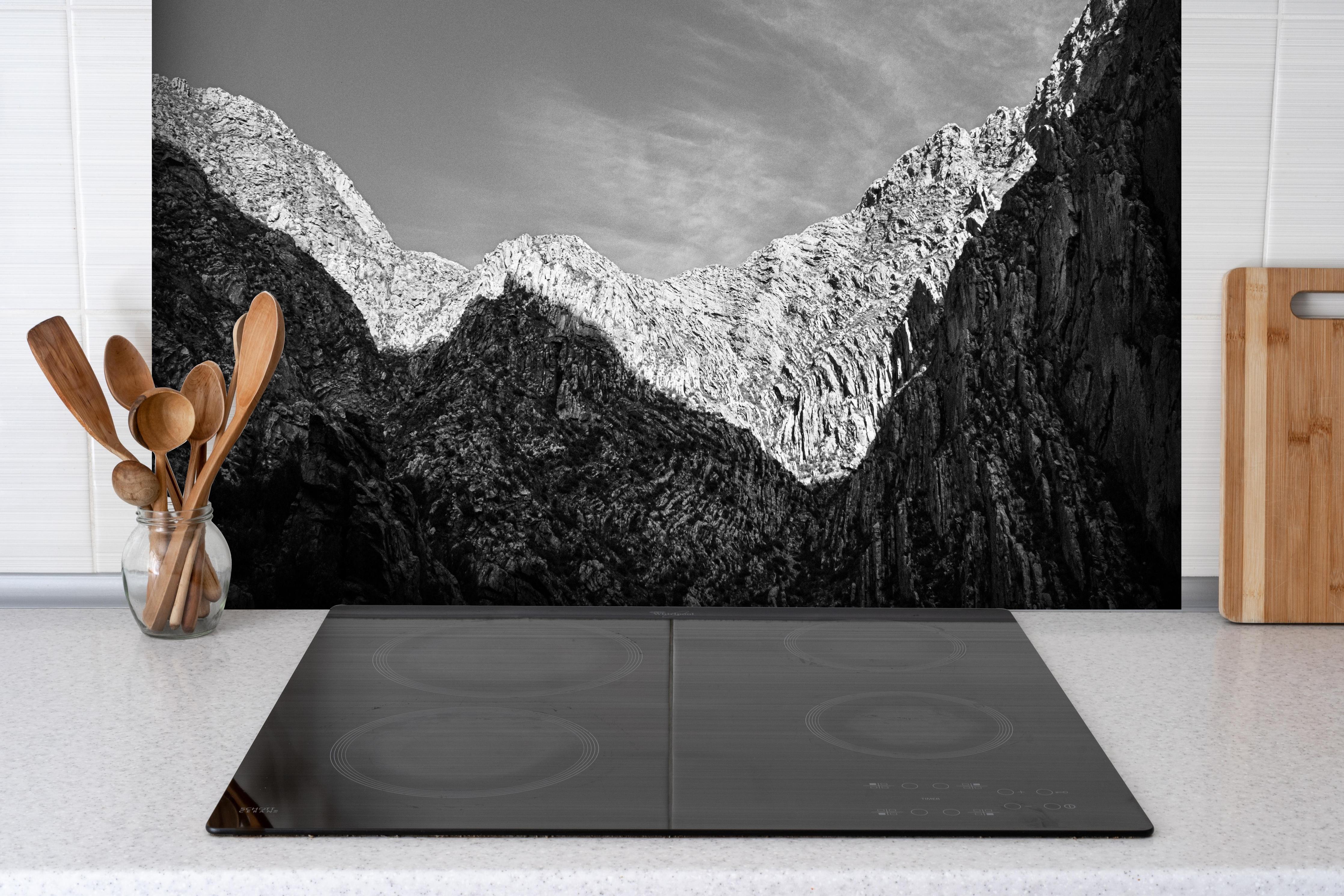Spritzschutz - Minimalistische Berglandschaft in Schwarz-Weiß hinter einem Cerankochfeld zwischen Holz-Kochutensilien