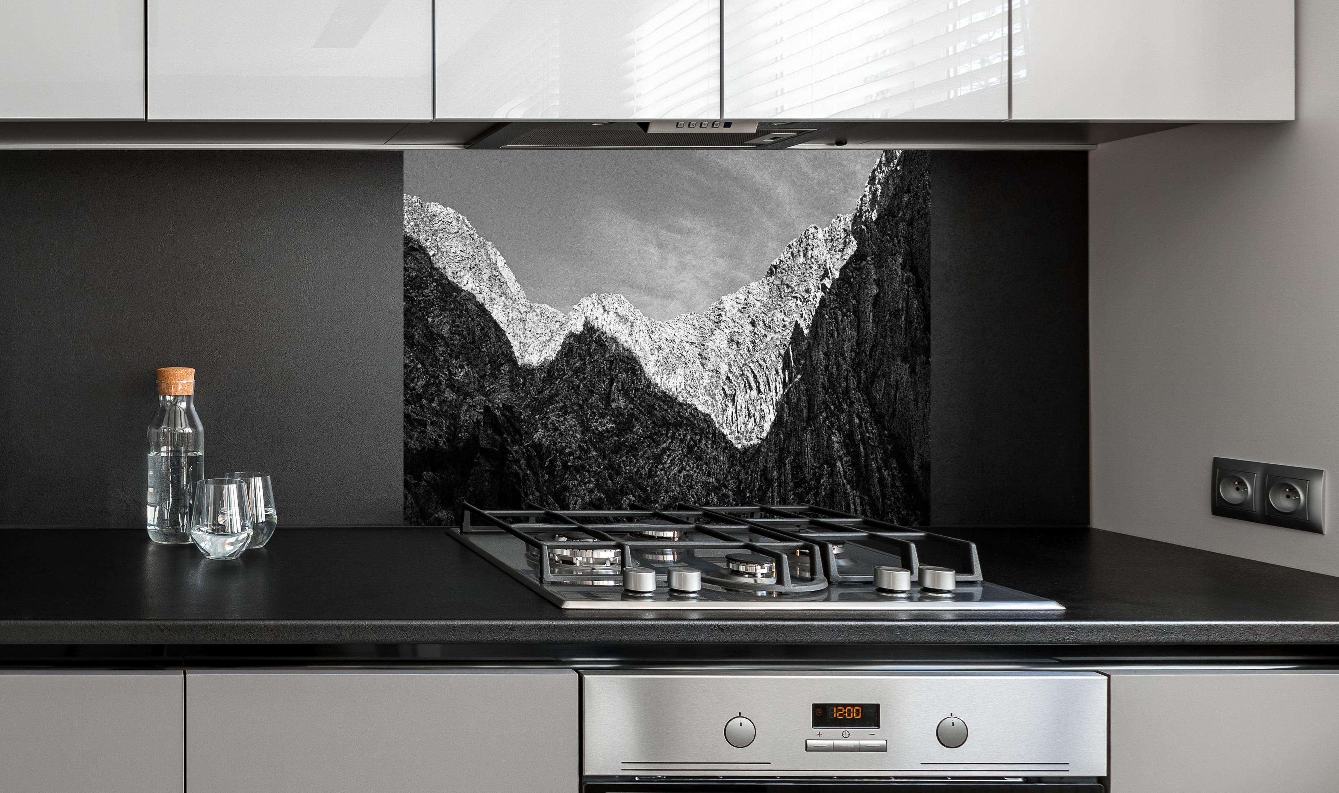 Spritzschutz - Minimalistische Berglandschaft in Schwarz-Weiß hinter einem Cerankochfeld zwischen Holz-Kochutensilien