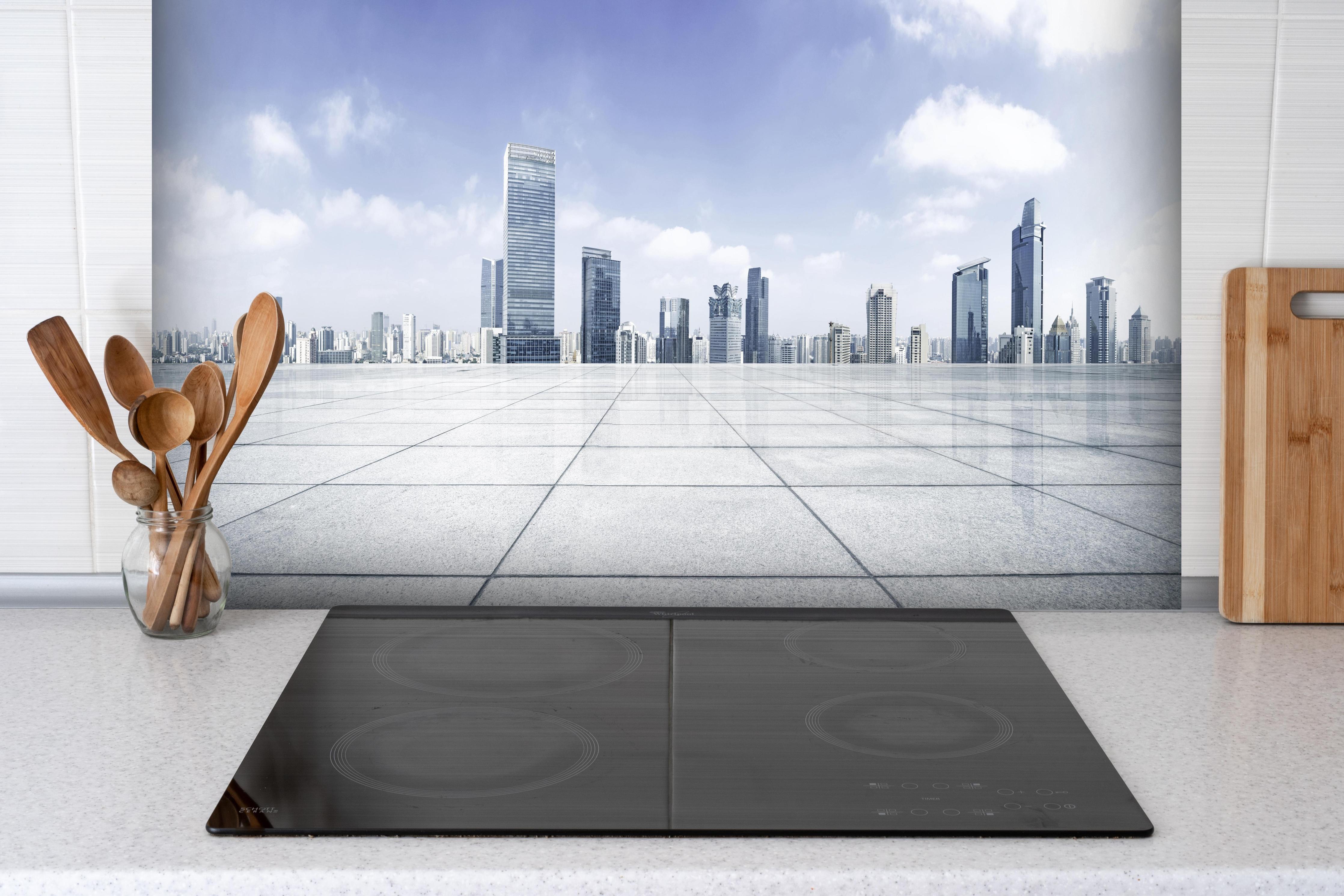 Spritzschutz - Moderner Skyline und Gebäuden hinter einem Cerankochfeld zwischen Holz-Kochutensilien