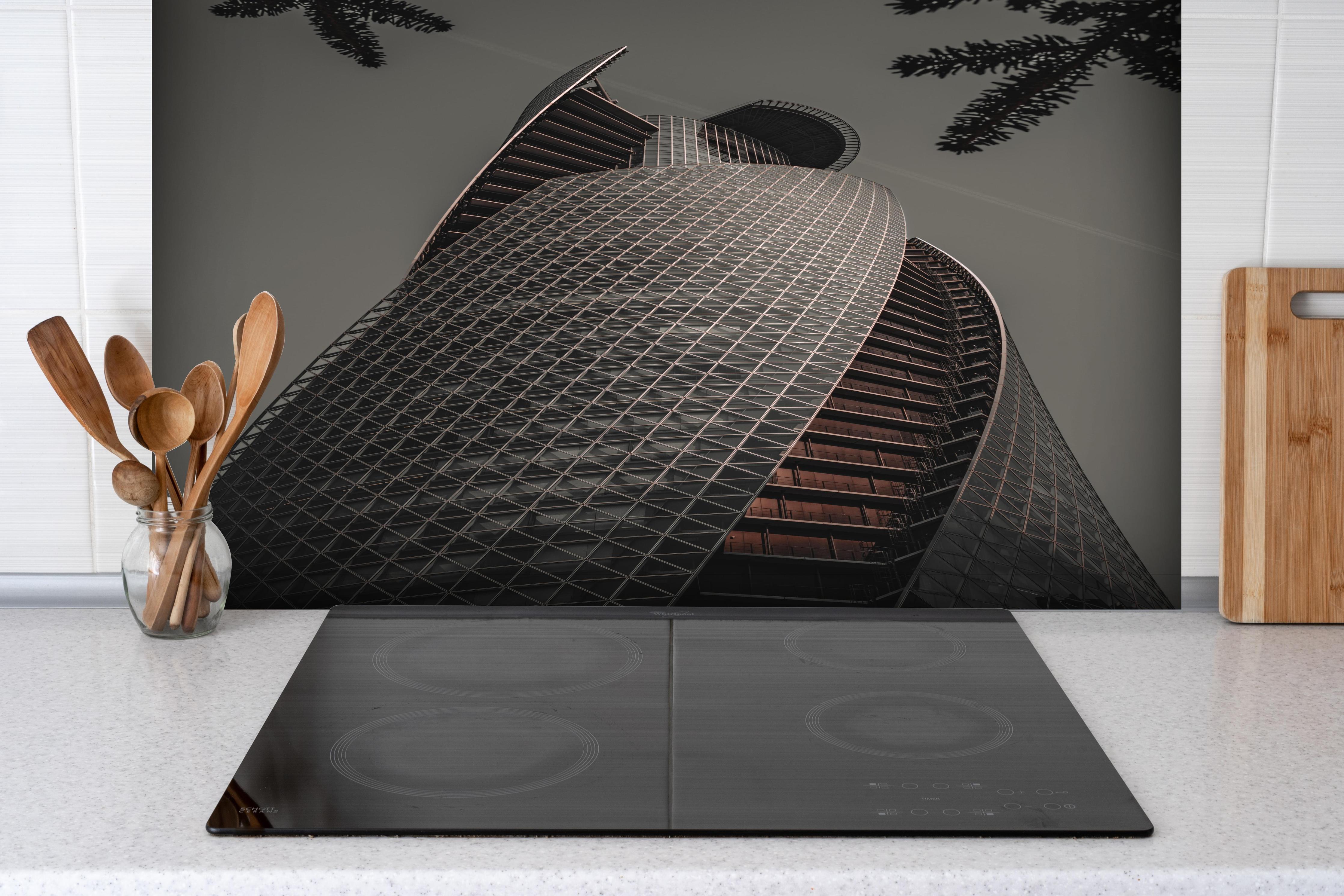 Spritzschutz - Modernes Spiral-Gebäude in Grautönen hinter einem Cerankochfeld zwischen Holz-Kochutensilien