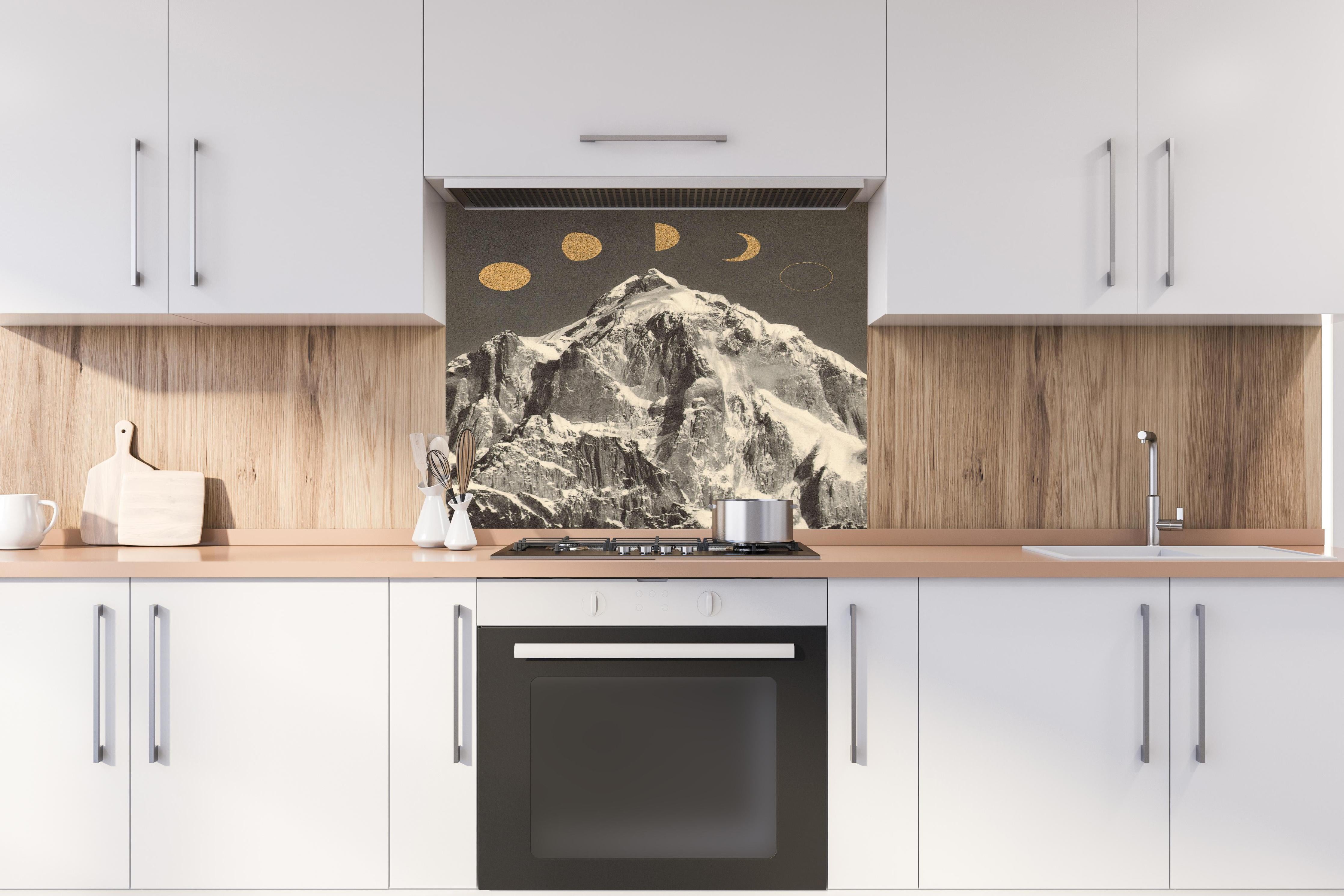 Spritzschutz - Monochrome Mondphasen über schneebedecktem Berg hinter einem Cerankochfeld zwischen Holz-Kochutensilien