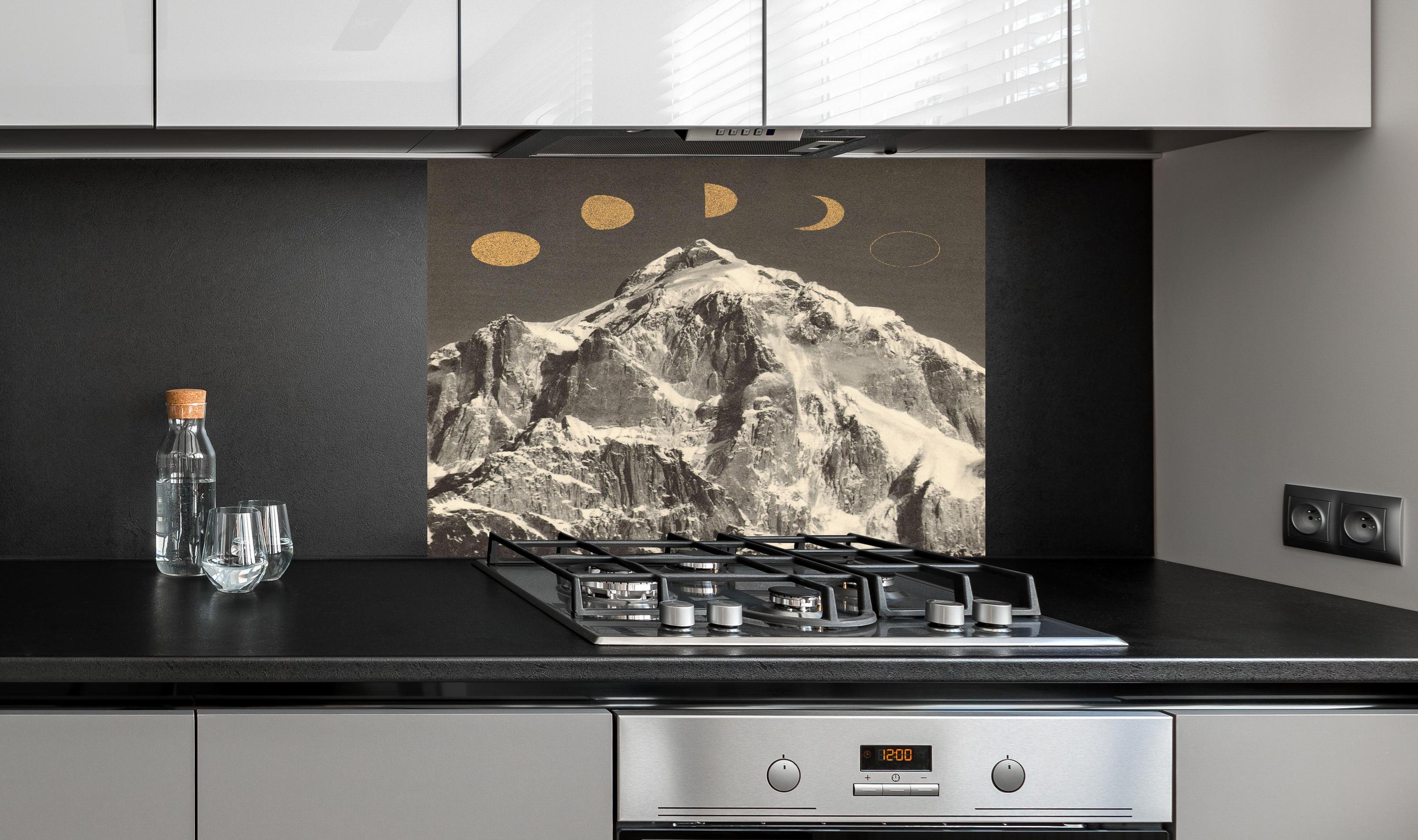 Spritzschutz - Monochrome Mondphasen über schneebedecktem Berg hinter einem Cerankochfeld zwischen Holz-Kochutensilien