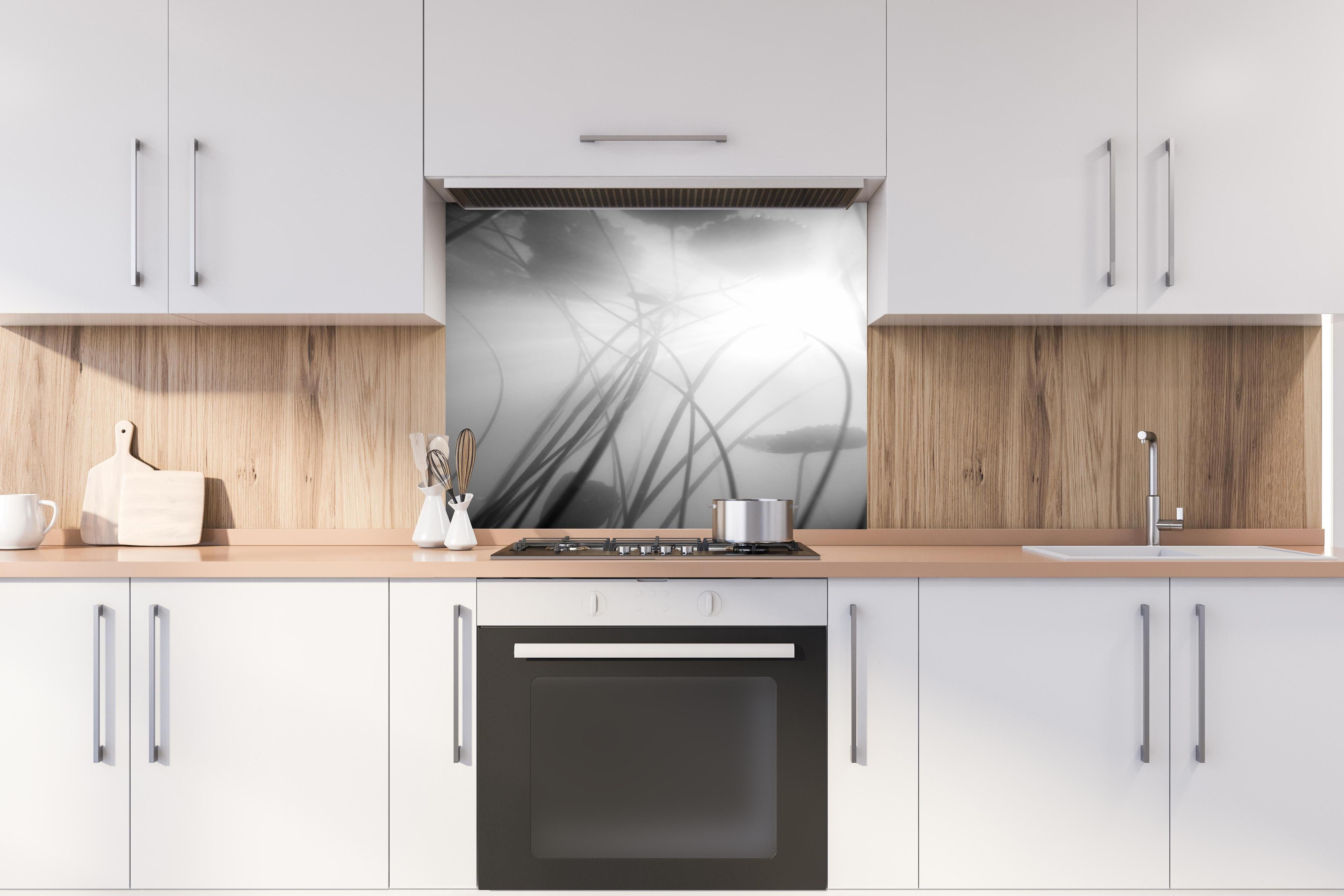 Spritzschutz - Monochrome Seerose mit dunkler Spiegelung hinter einem Cerankochfeld zwischen Holz-Kochutensilien