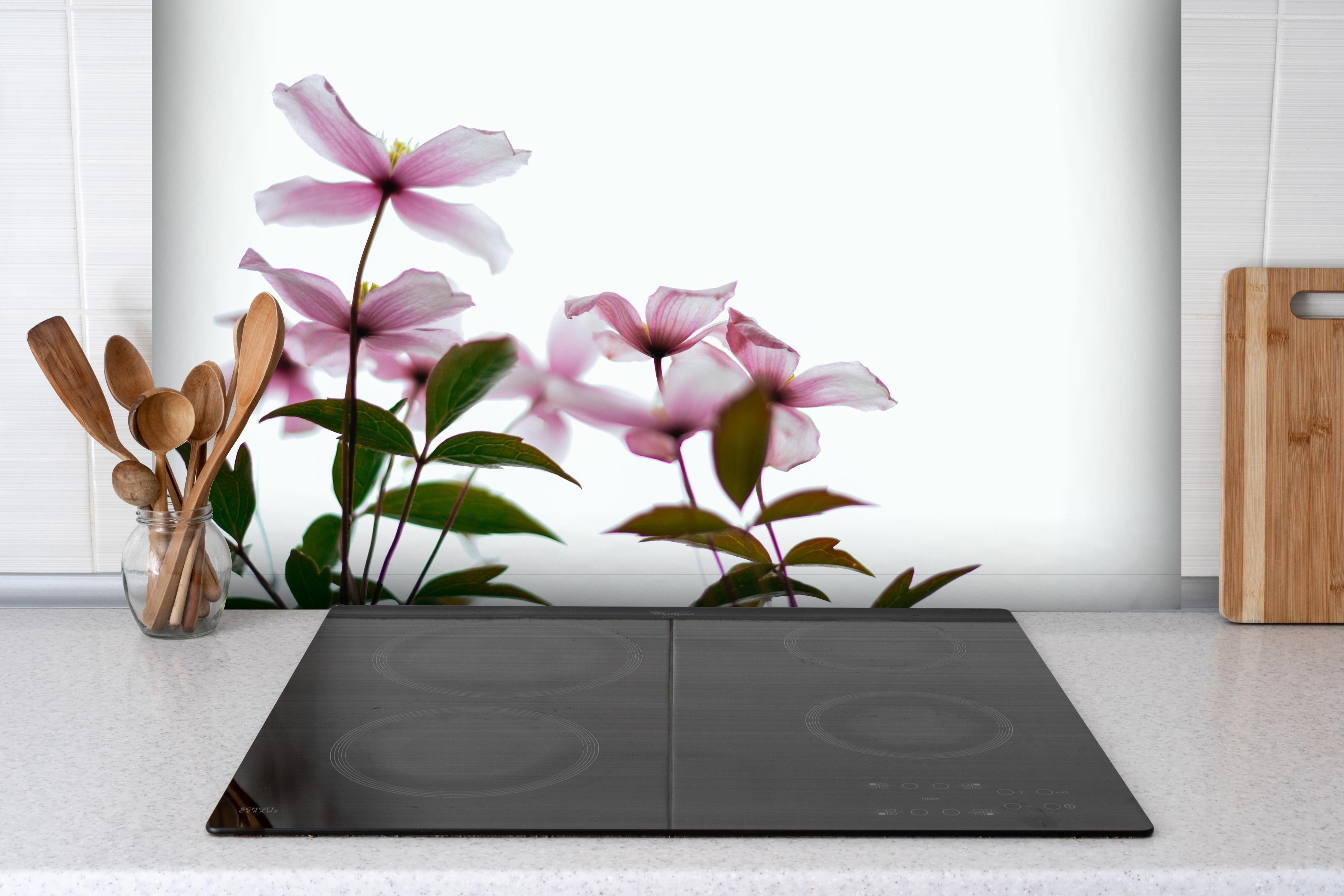 Spritzschutz - Nahaufnahme - Clematis Blüten hinter einem Cerankochfeld zwischen Holz-Kochutensilien