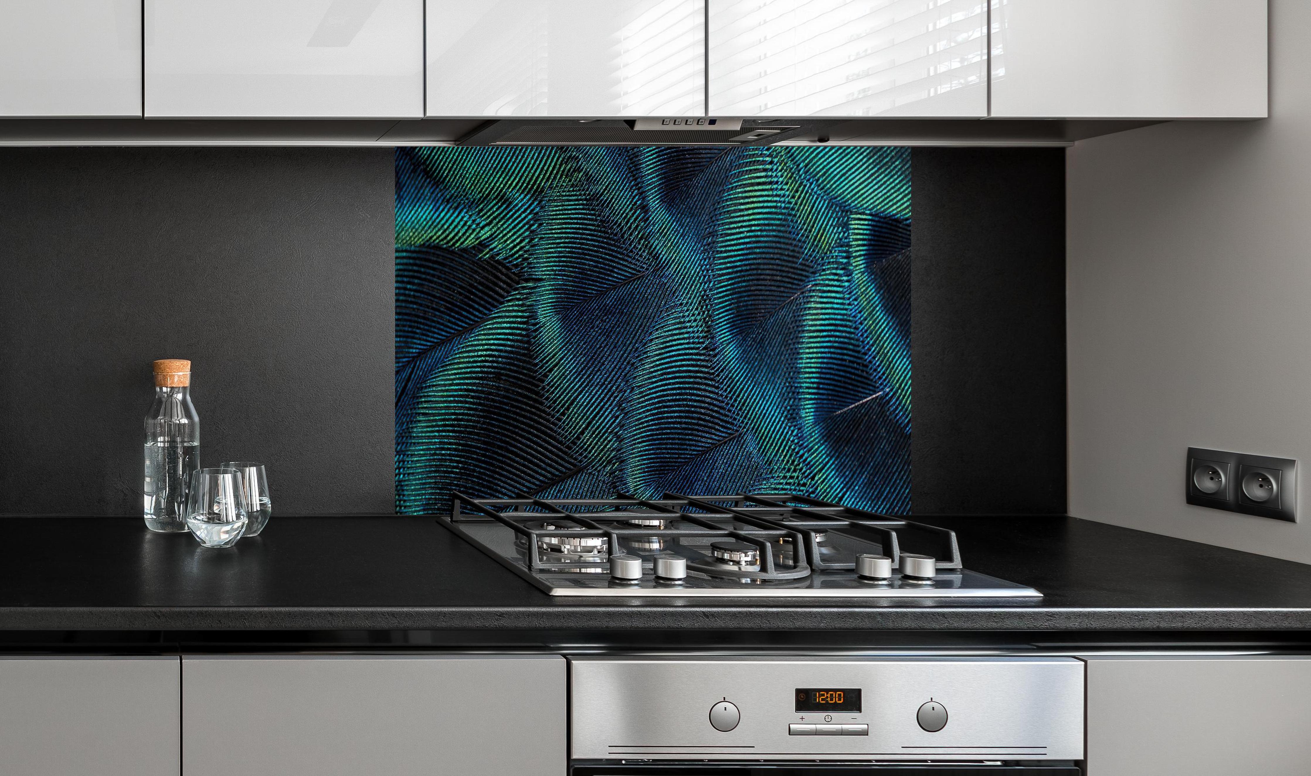 Spritzschutz - Nahaufnahme von Pfauenfedern hinter einem Cerankochfeld zwischen Holz-Kochutensilien