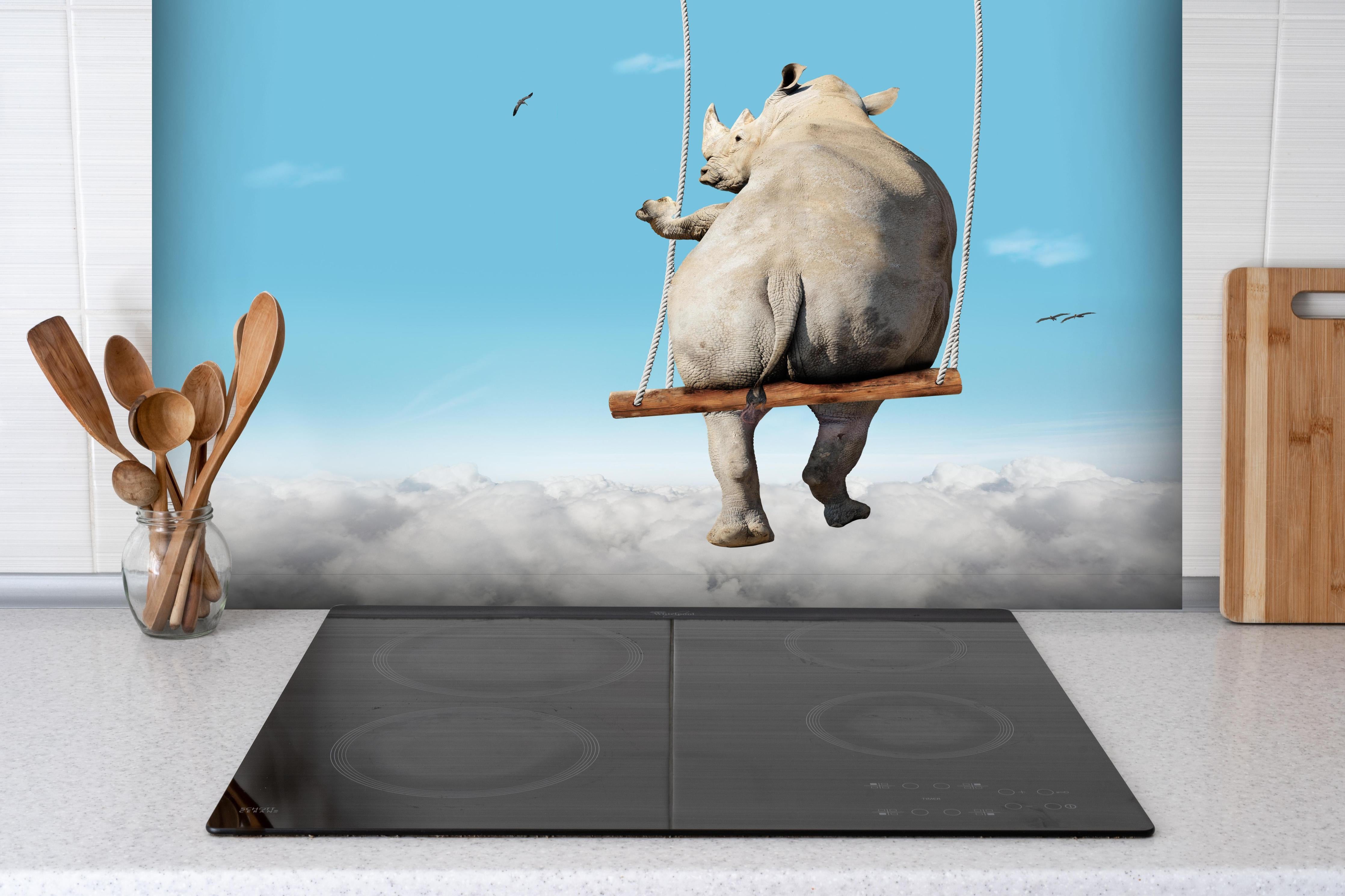 Spritzschutz - Nashorn schaukelt über den Wolken hinter einem Cerankochfeld zwischen Holz-Kochutensilien