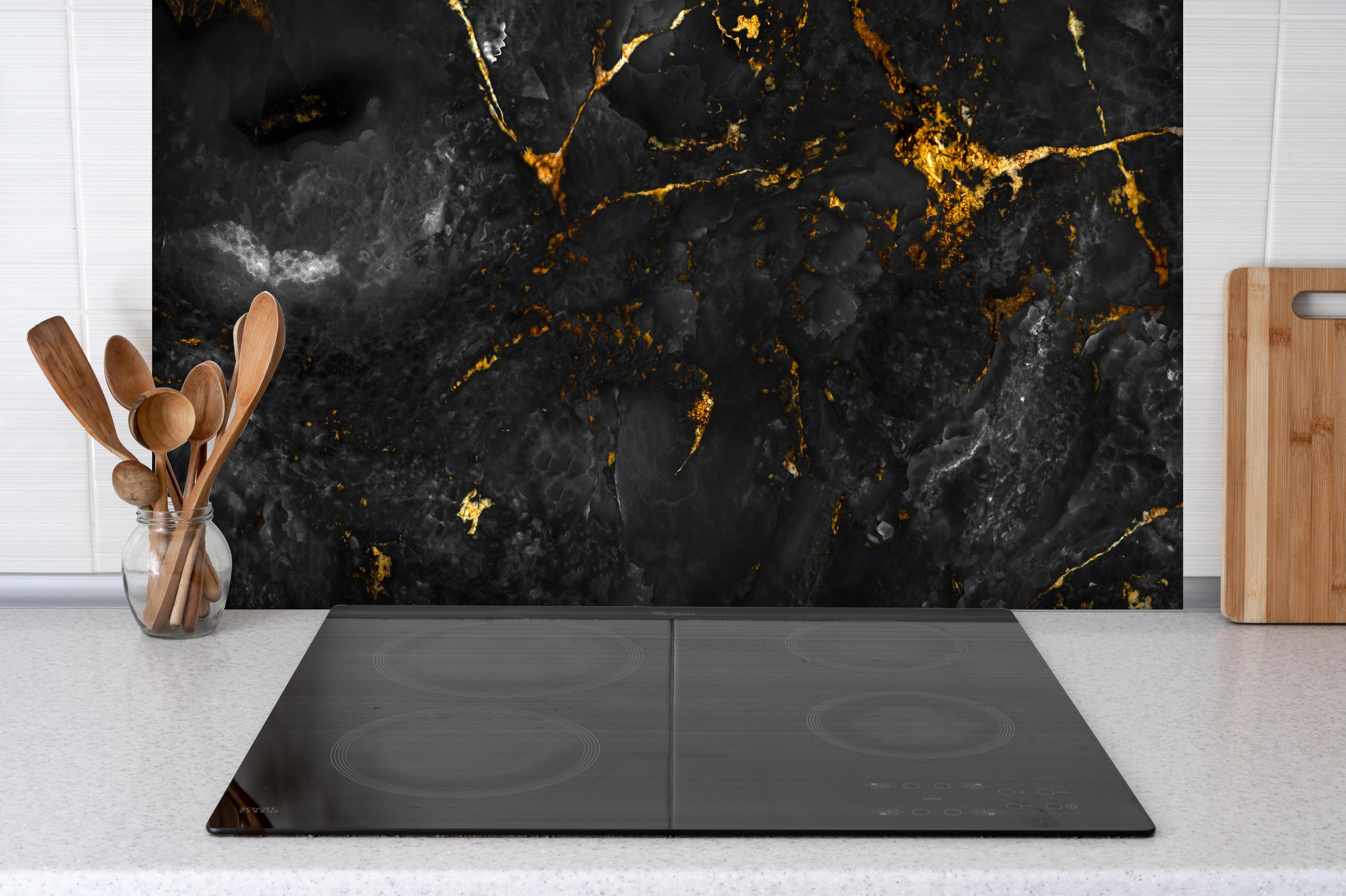 Spritzschutz - Natürliche schwarze Marmorstruktur mit goldenen Adern hinter einem Cerankochfeld zwischen Holz-Kochutensilien
