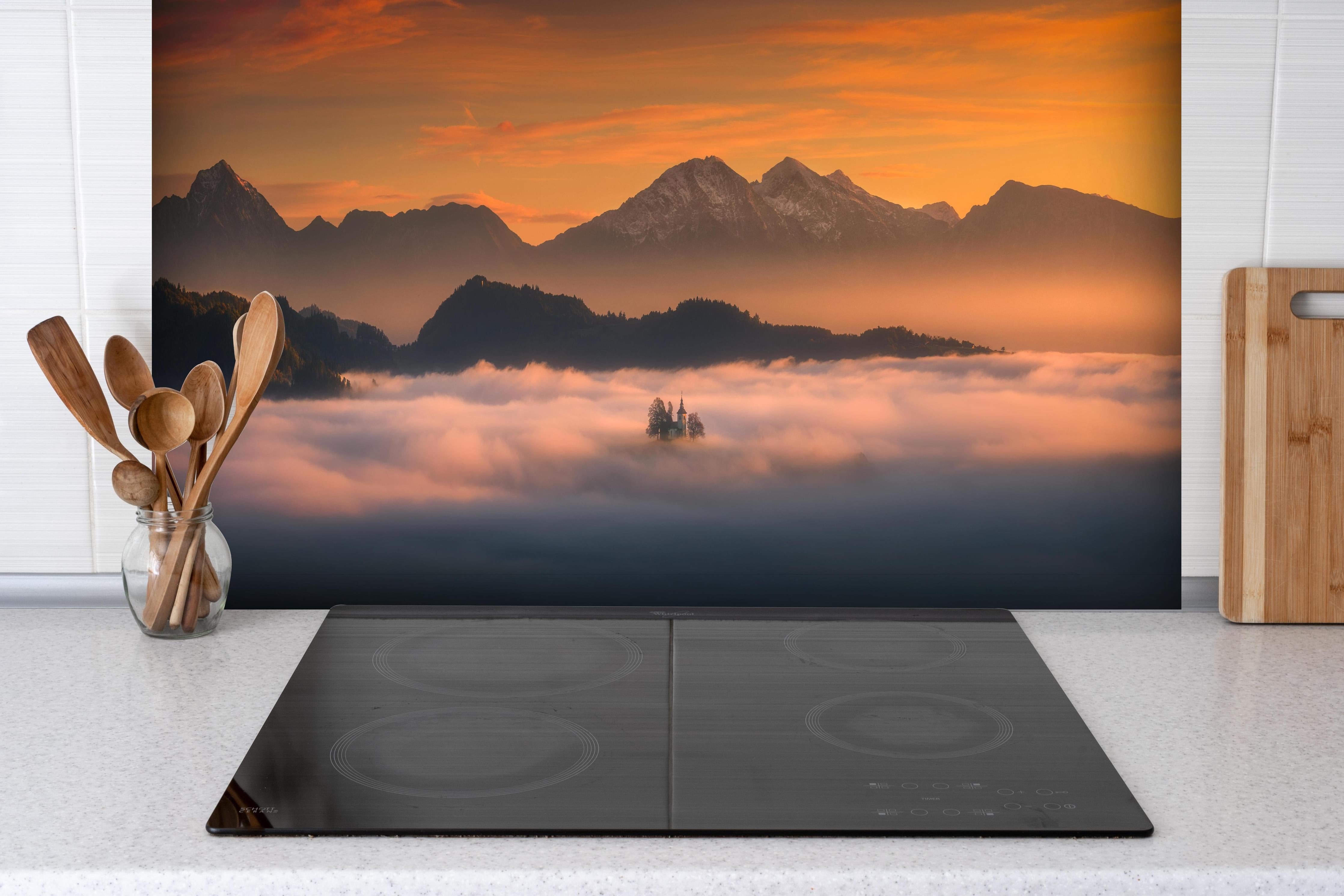 Spritzschutz - Nebelverhangene Berge bei Sonnenaufgang hinter einem Cerankochfeld zwischen Holz-Kochutensilien