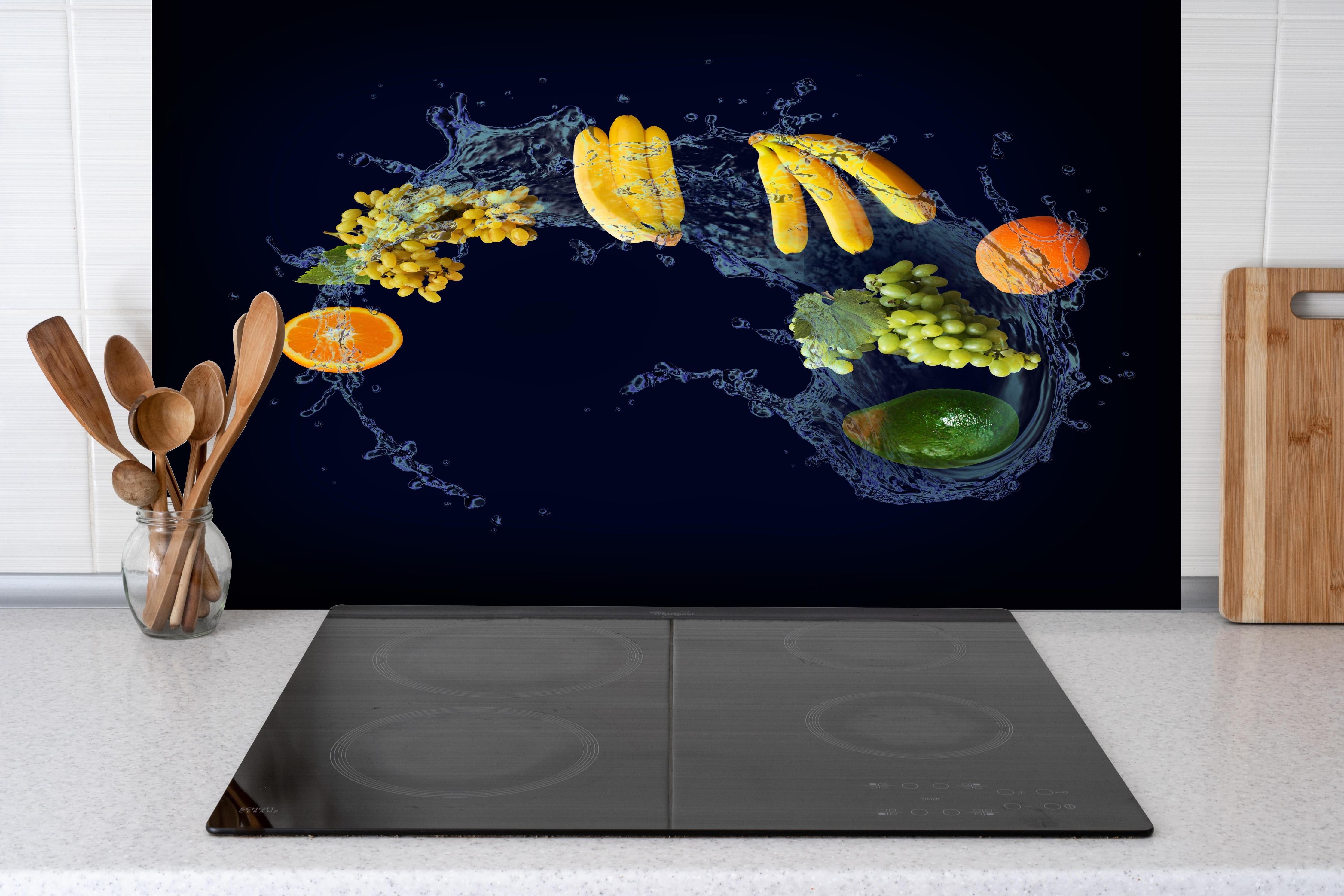 Spritzschutz - Obstsorten mit blauen Wasserspritzern hinter einem Cerankochfeld zwischen Holz-Kochutensilien