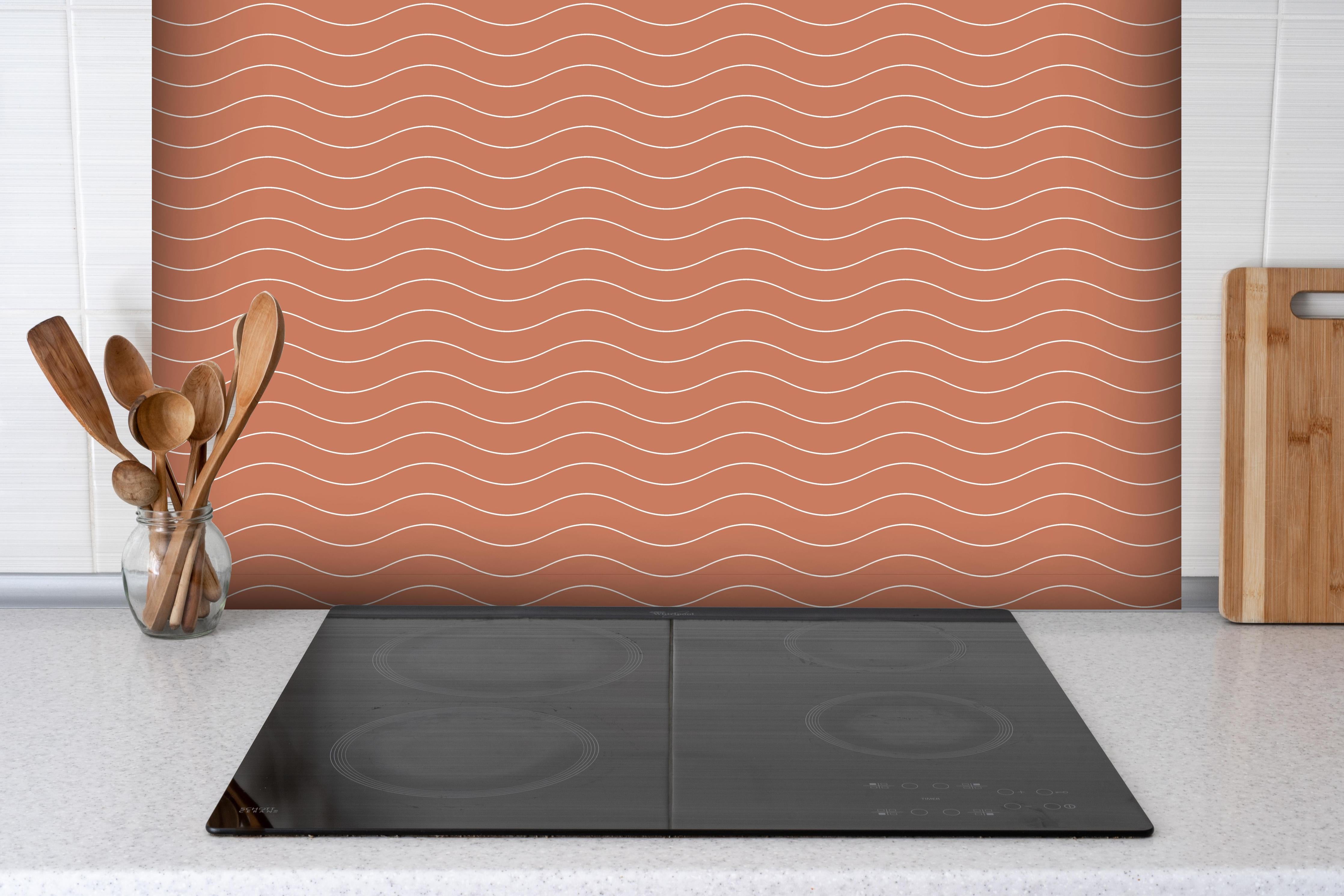 Spritzschutz - Onde Abisso Terracotta hinter einem Cerankochfeld zwischen Holz-Kochutensilien
