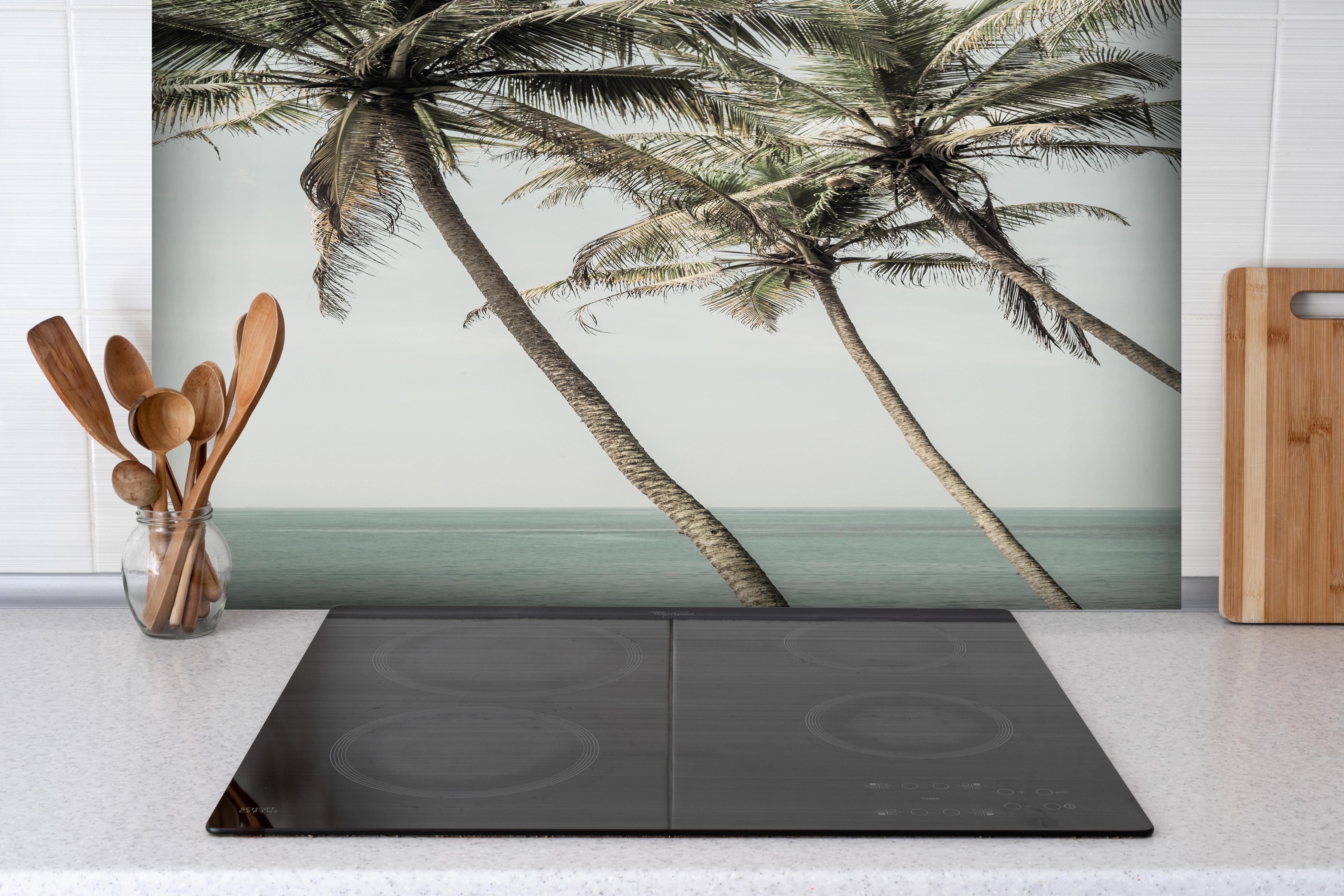 Spritzschutz - Palmen am Meer hinter einem Cerankochfeld zwischen Holz-Kochutensilien