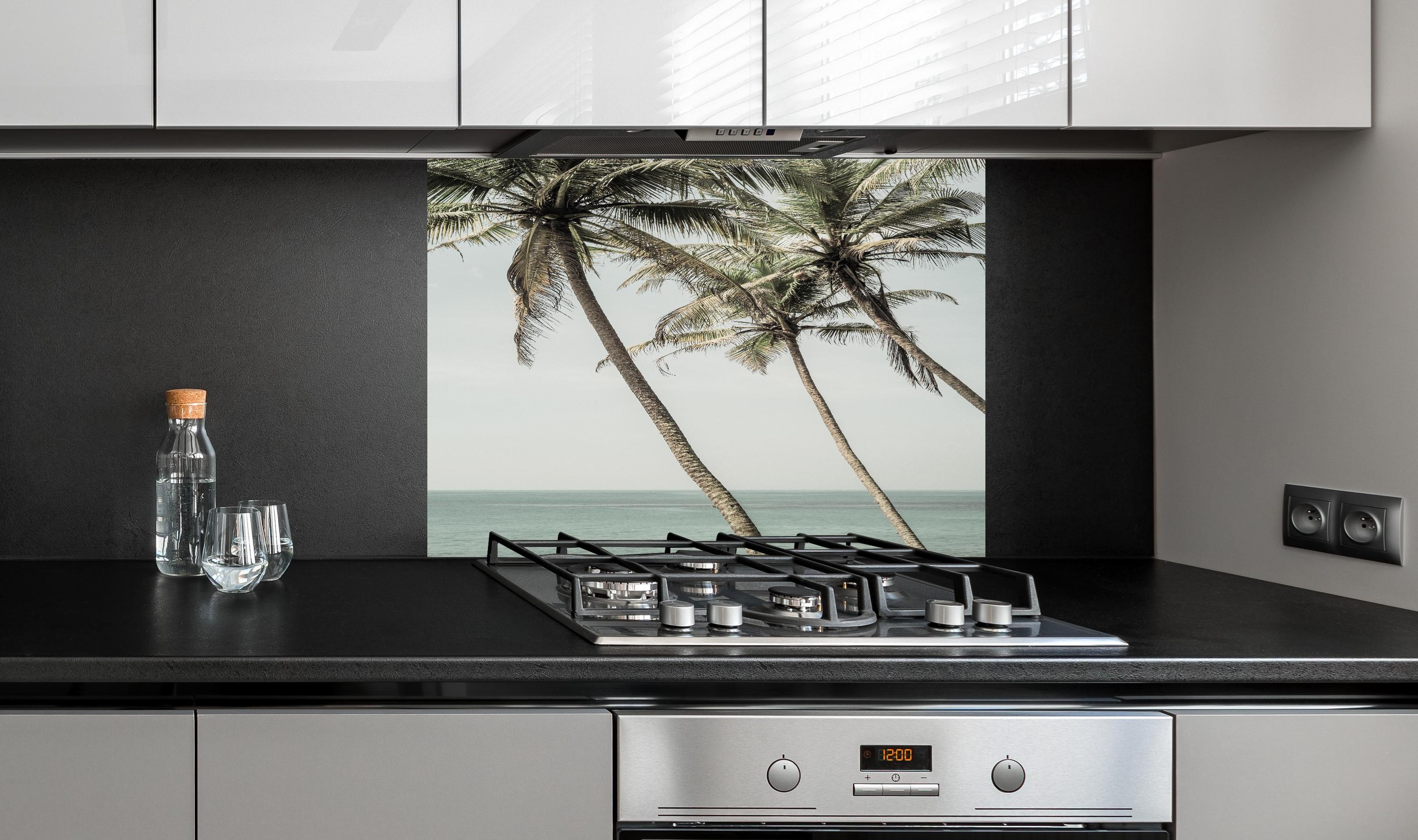 Spritzschutz - Palmen am Meer hinter einem Cerankochfeld zwischen Holz-Kochutensilien