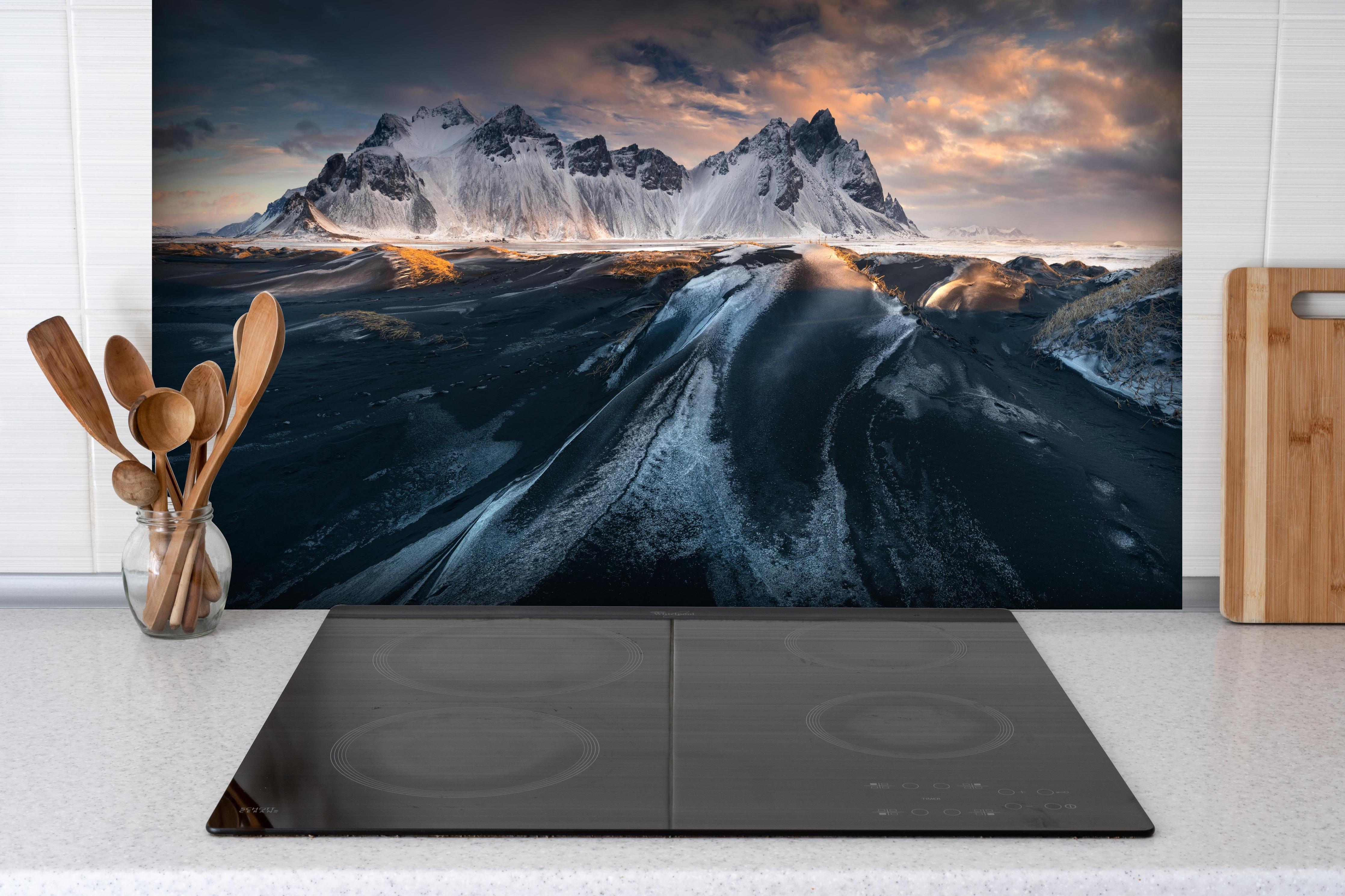 Spritzschutz - Panorama Schneebedeckter Berge bei Sonnenuntergang hinter einem Cerankochfeld zwischen Holz-Kochutensilien