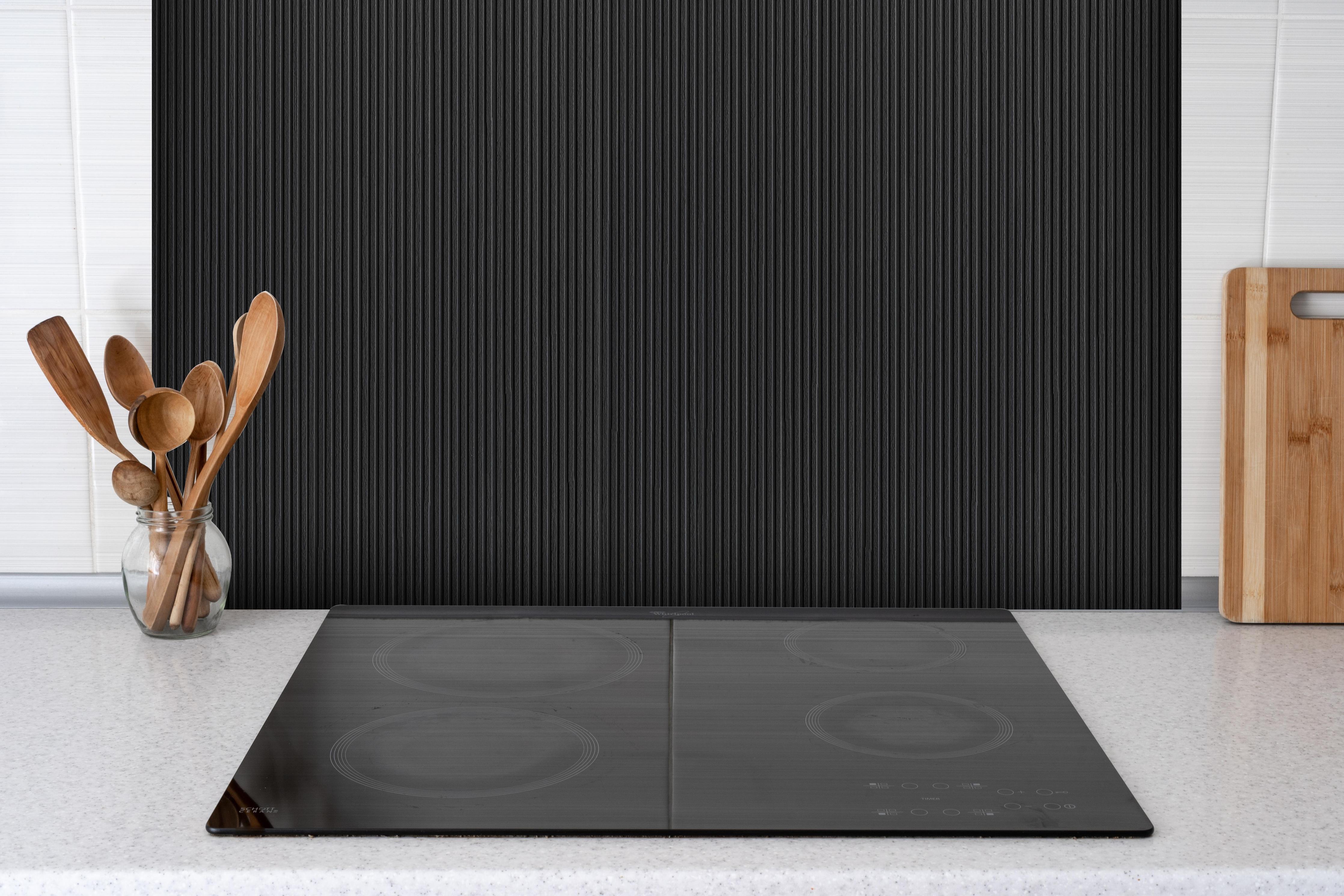 Spritzschutz - Panorama der schwarzen Holzplanke hinter einem Cerankochfeld zwischen Holz-Kochutensilien