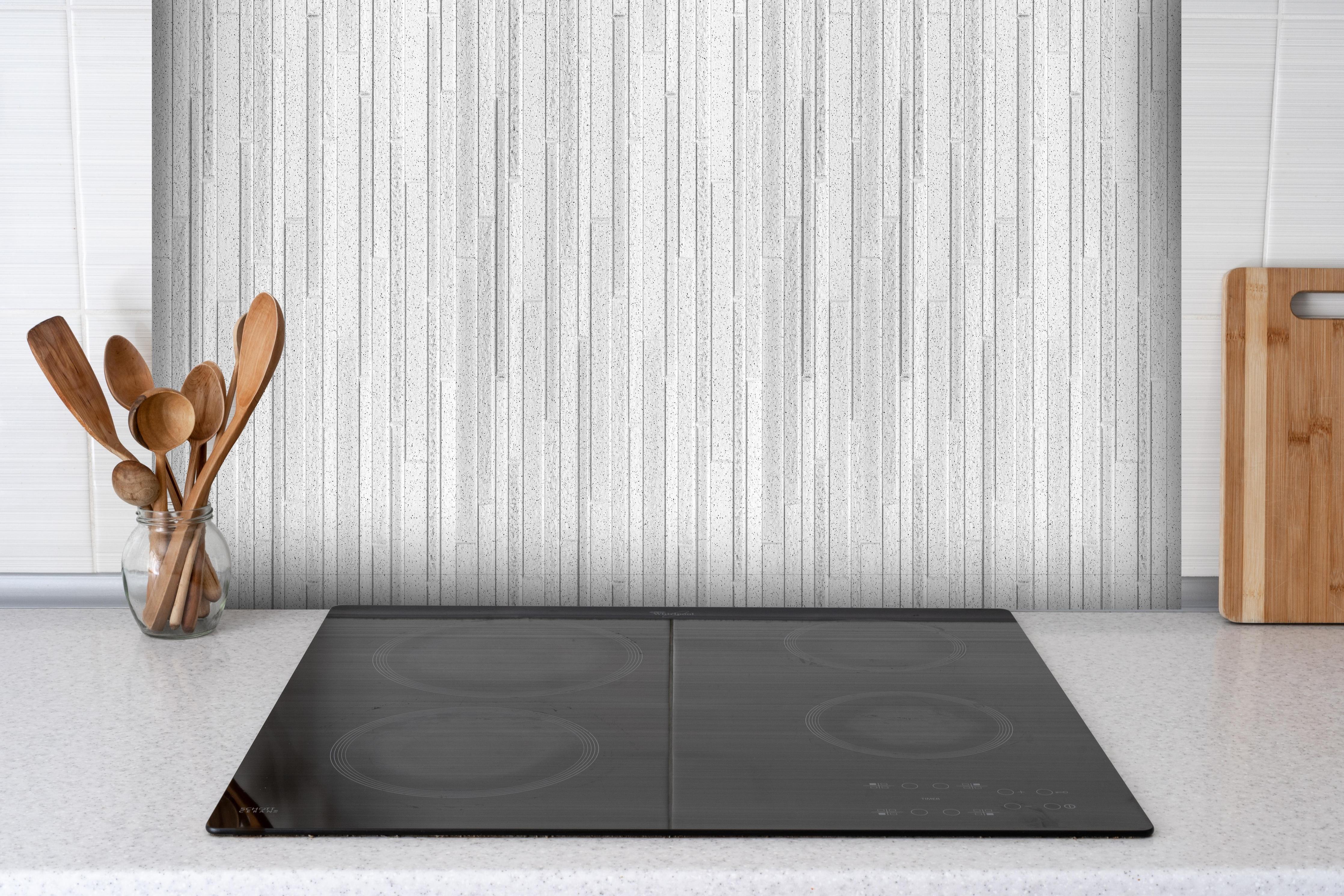 Spritzschutz - Panorama der weißen Granitblockwand hinter einem Cerankochfeld zwischen Holz-Kochutensilien