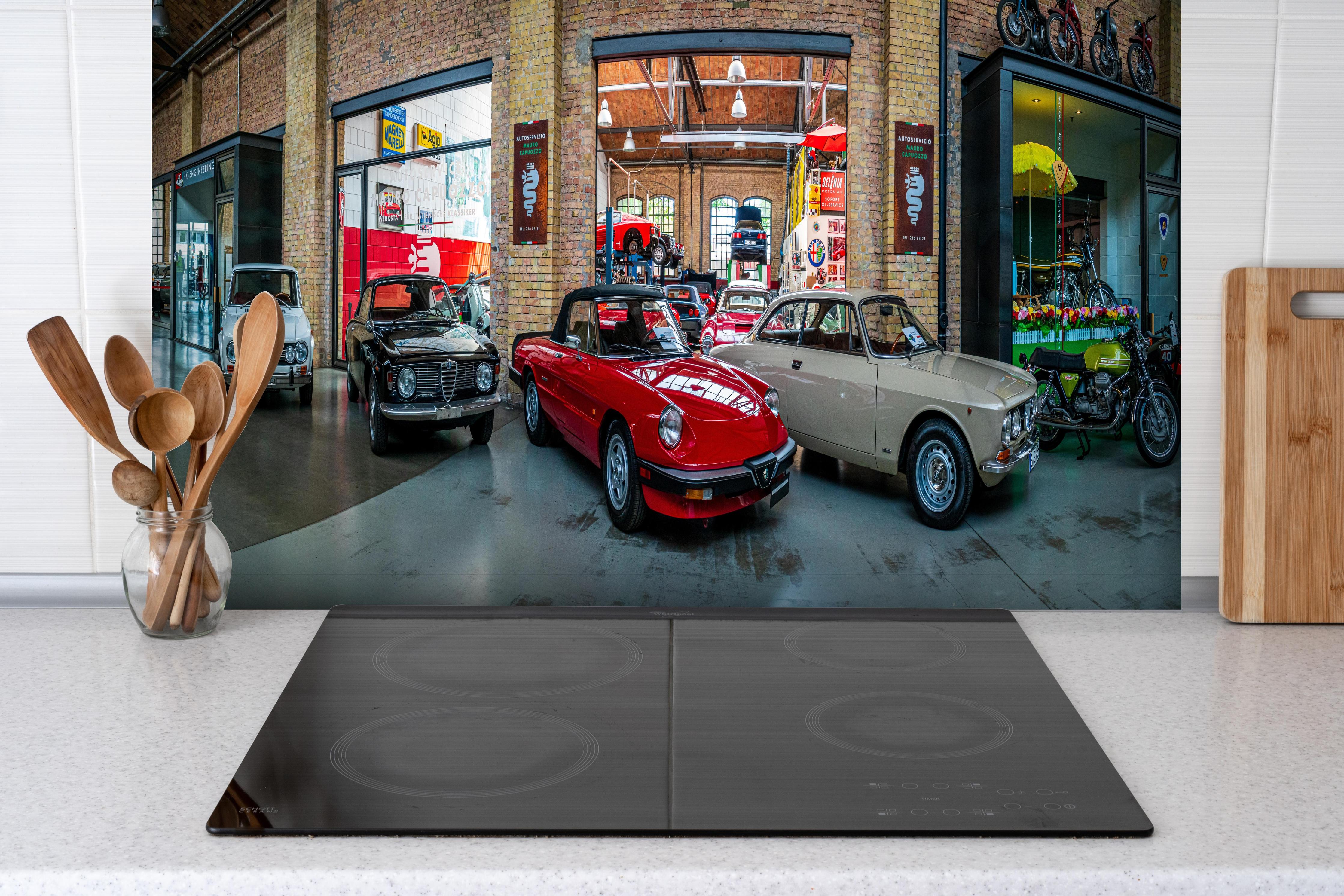 Spritzschutz - Panoramablick auf die Werkstatt der Classic Remise Berlin hinter einem Cerankochfeld zwischen Holz-Kochutensilien