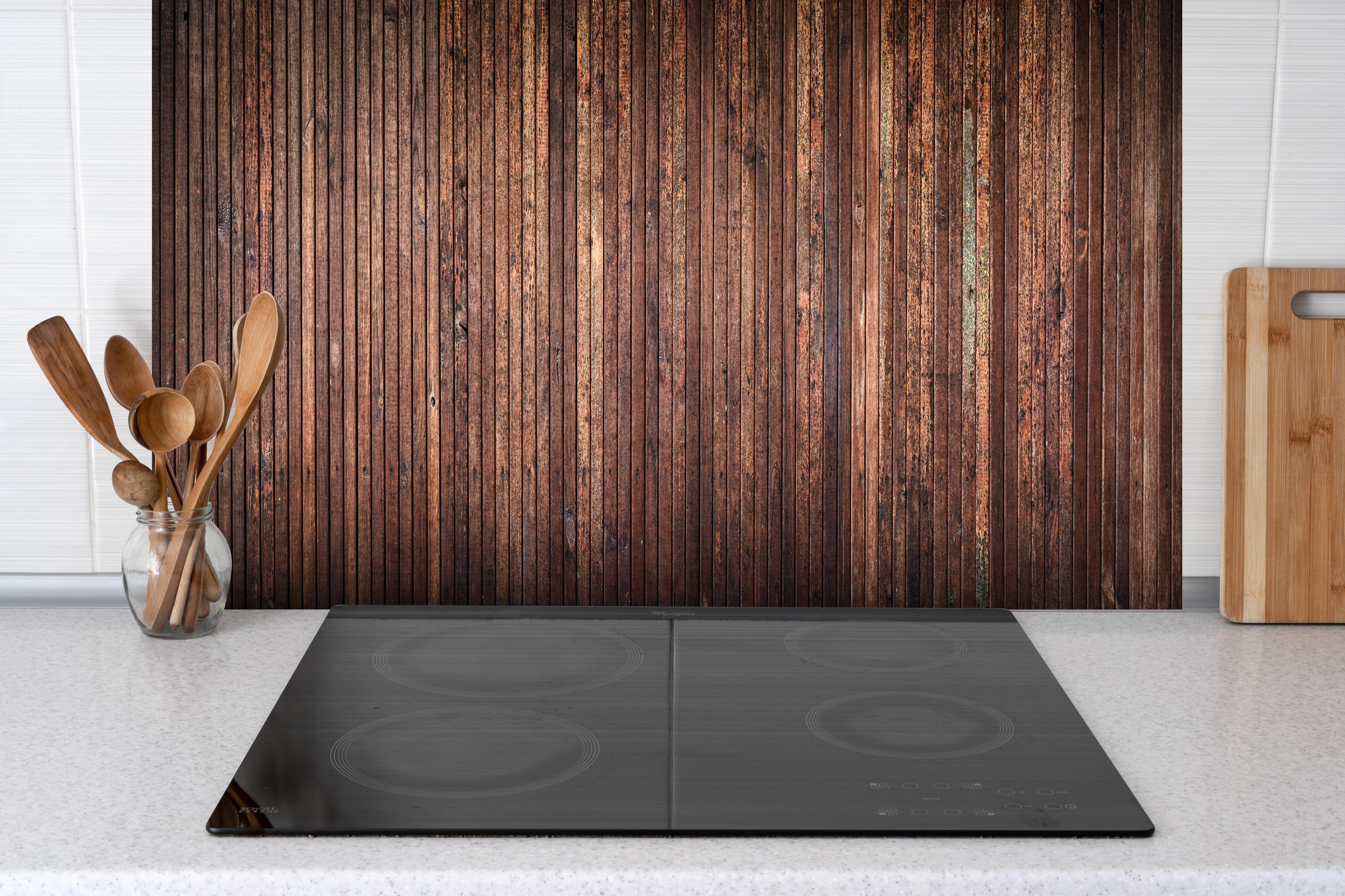 Spritzschutz - Panoramahintergrund aus vertikalen schmalen Holzplatten hinter einem Cerankochfeld zwischen Holz-Kochutensilien