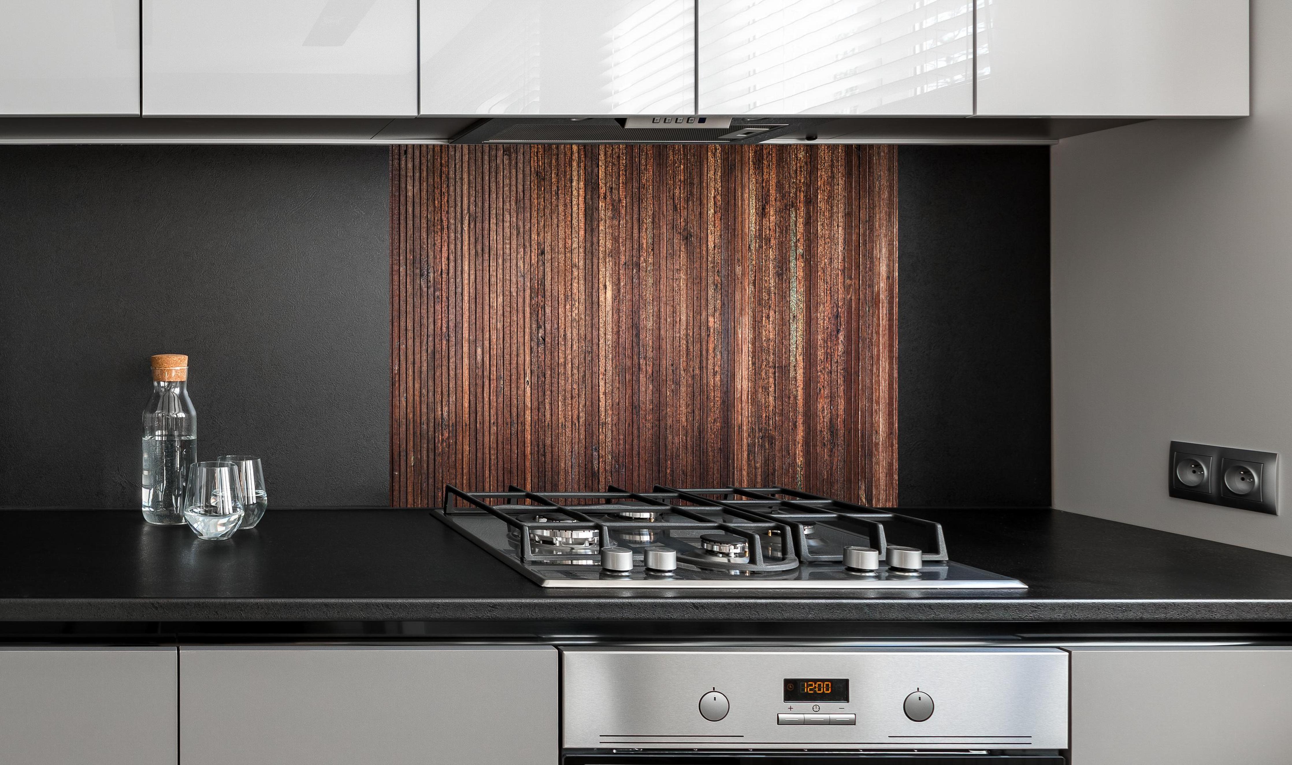 Spritzschutz - Panoramahintergrund aus vertikalen schmalen Holzplatten hinter einem Cerankochfeld zwischen Holz-Kochutensilien