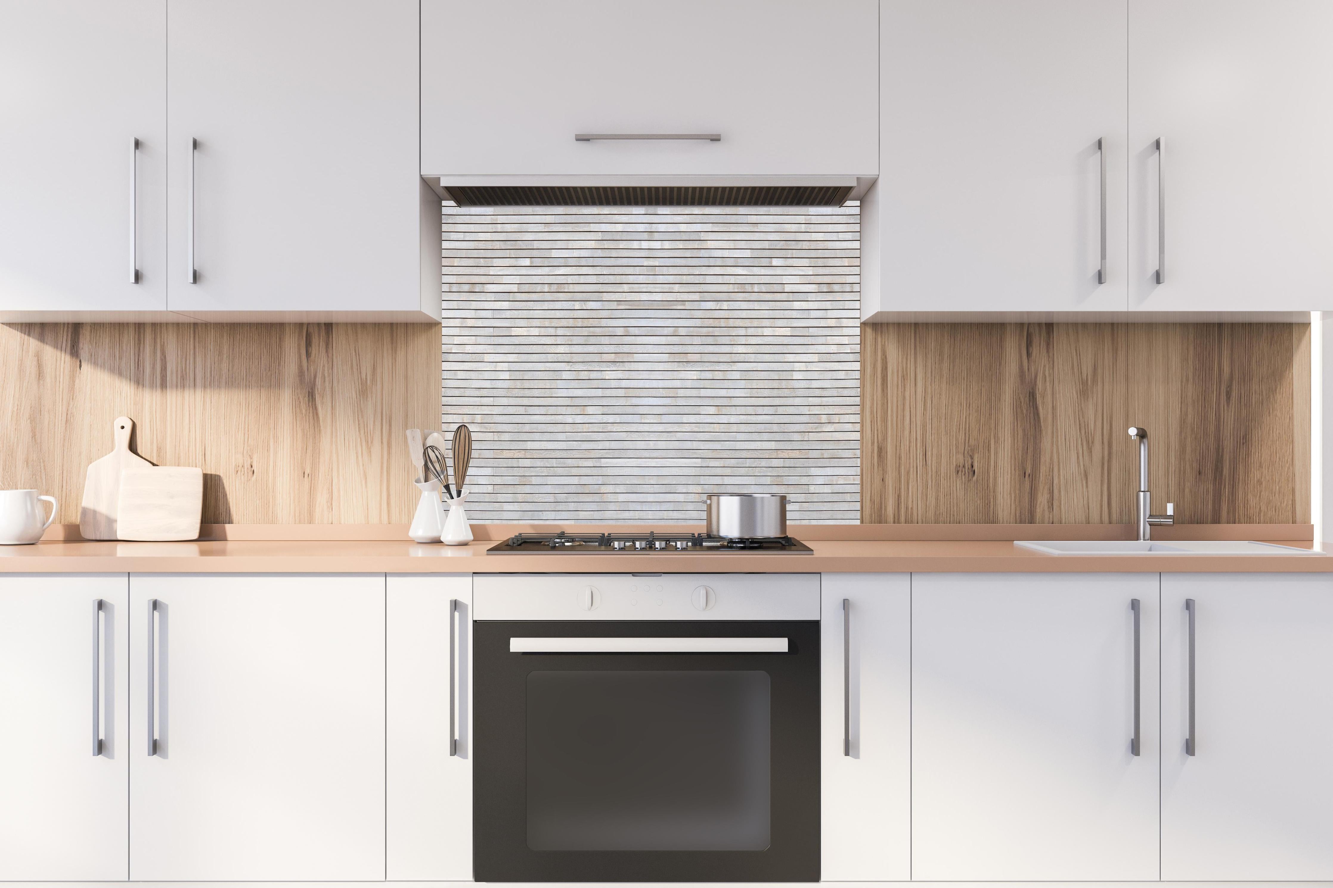 Spritzschutz - Pastellfarbige Holzfassade hinter einem Cerankochfeld zwischen Holz-Kochutensilien