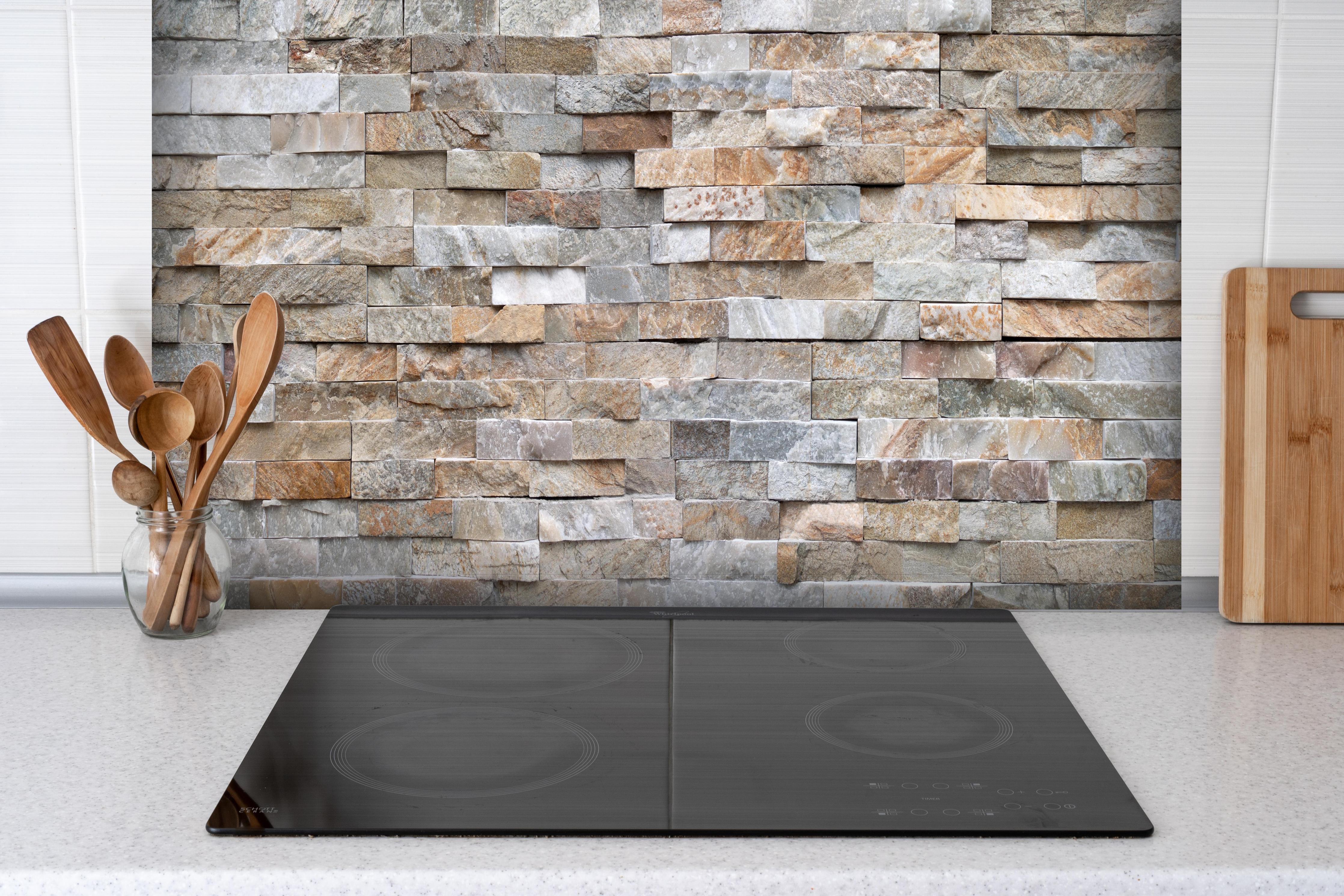 Spritzschutz - Pastellfarbige Steinmauer hinter einem Cerankochfeld zwischen Holz-Kochutensilien