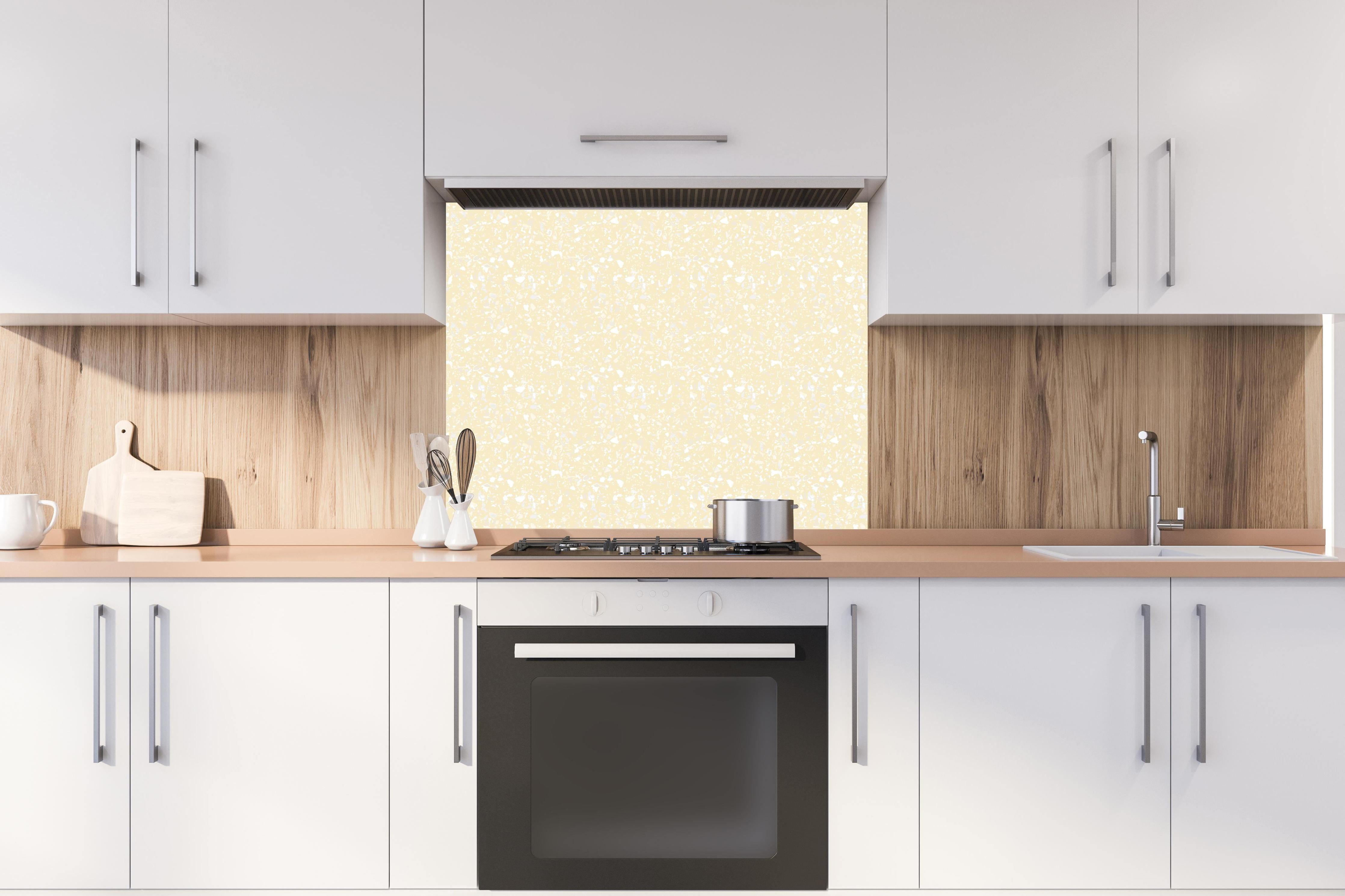 Spritzschutz - Pietre Terrazzo Avorio hinter einem Cerankochfeld zwischen Holz-Kochutensilien
