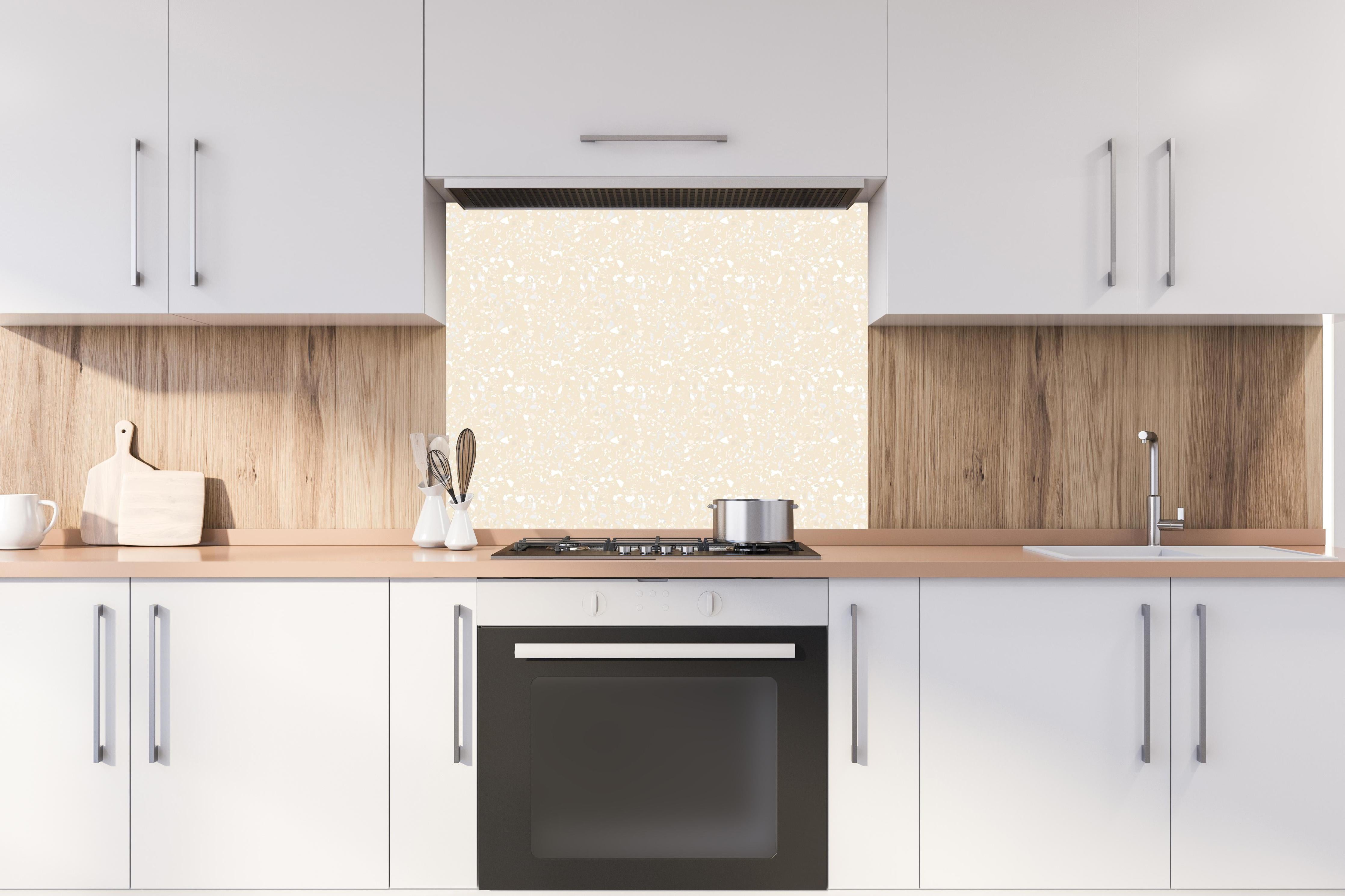 Spritzschutz - Pietre Terrazzo Crema hinter einem Cerankochfeld zwischen Holz-Kochutensilien