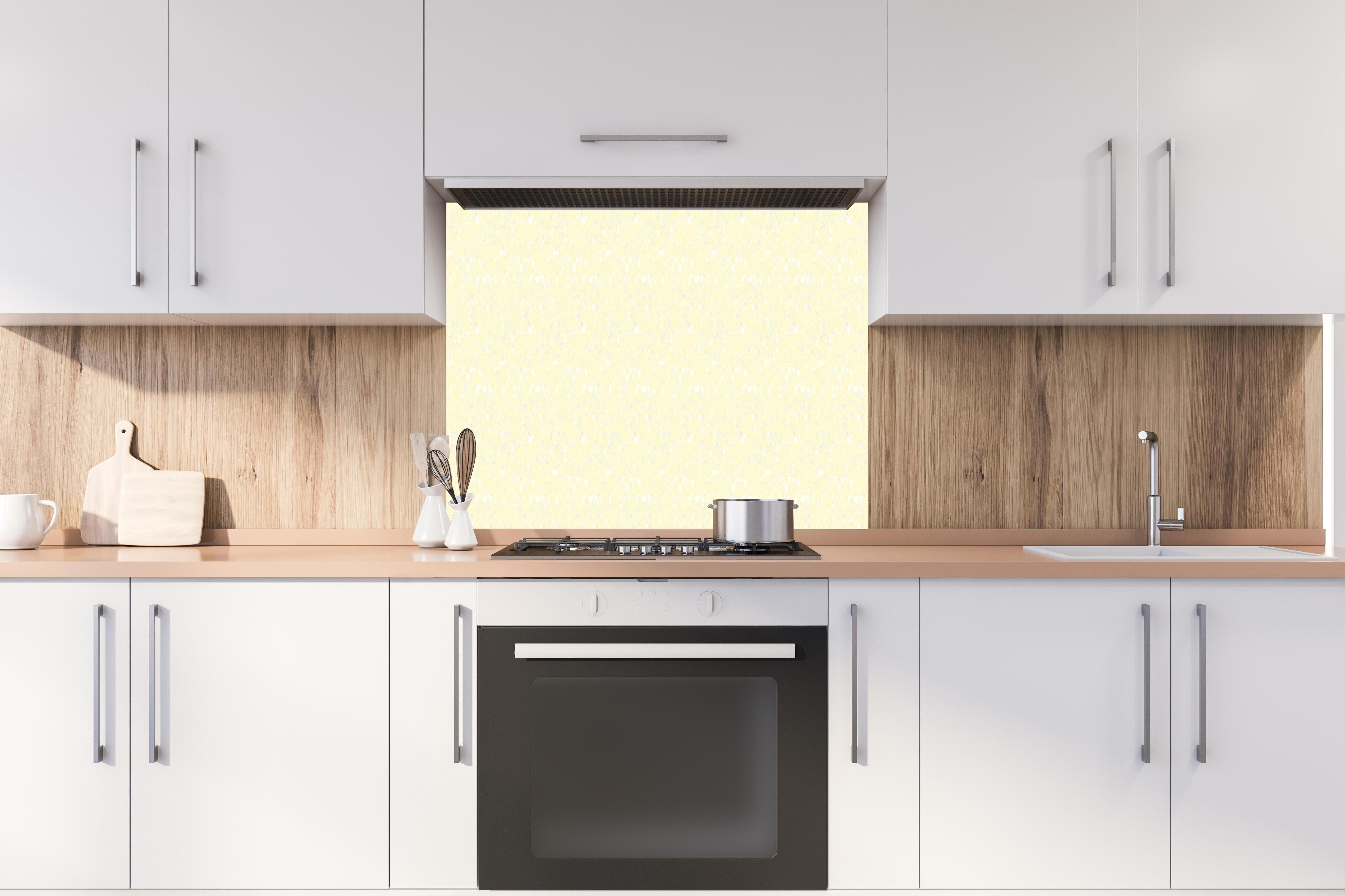 Spritzschutz - Pietre Terrazzo Limone crema hinter einem Cerankochfeld zwischen Holz-Kochutensilien