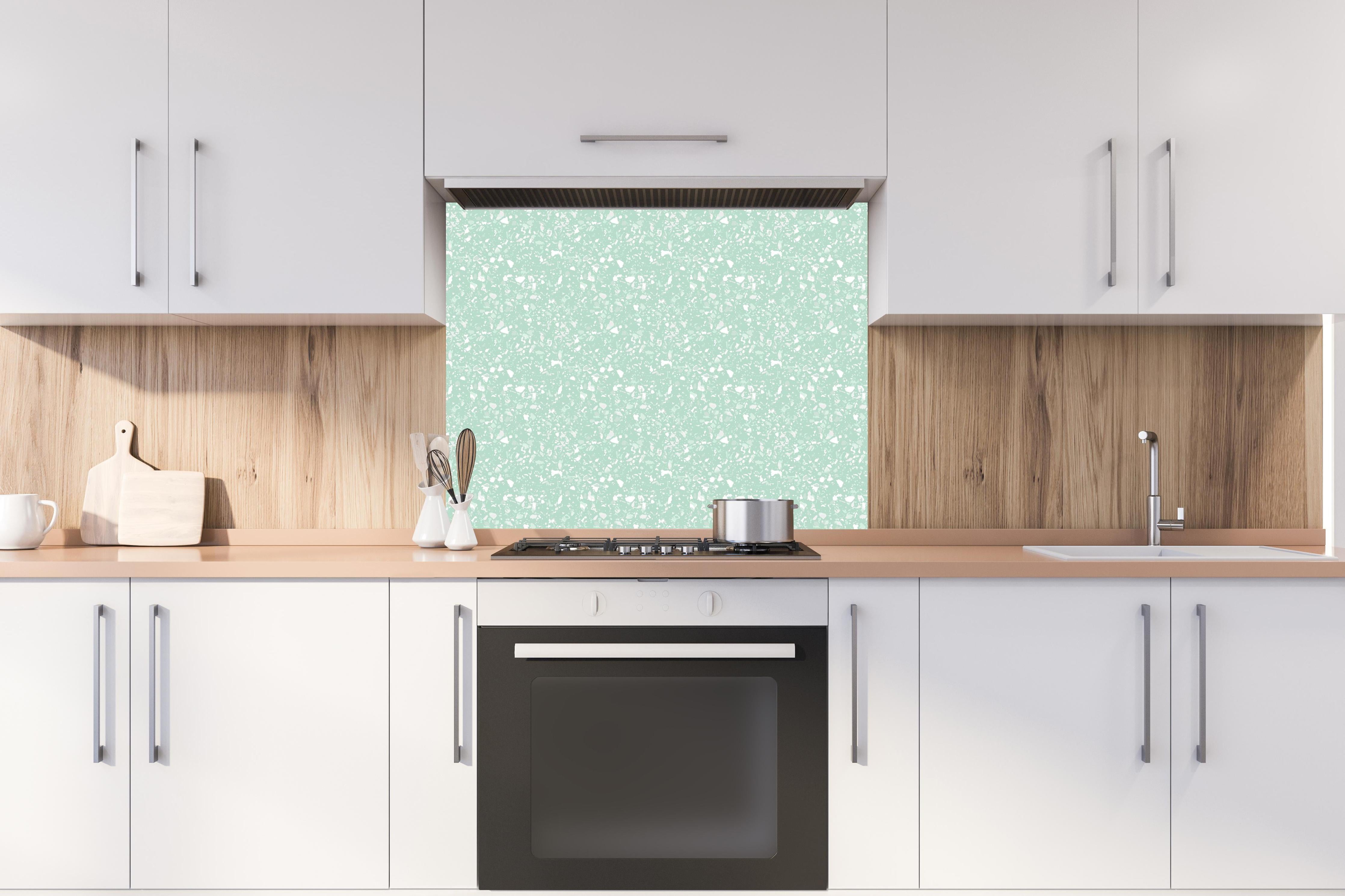 Spritzschutz - Pietre Terrazzo Menta hinter einem Cerankochfeld zwischen Holz-Kochutensilien