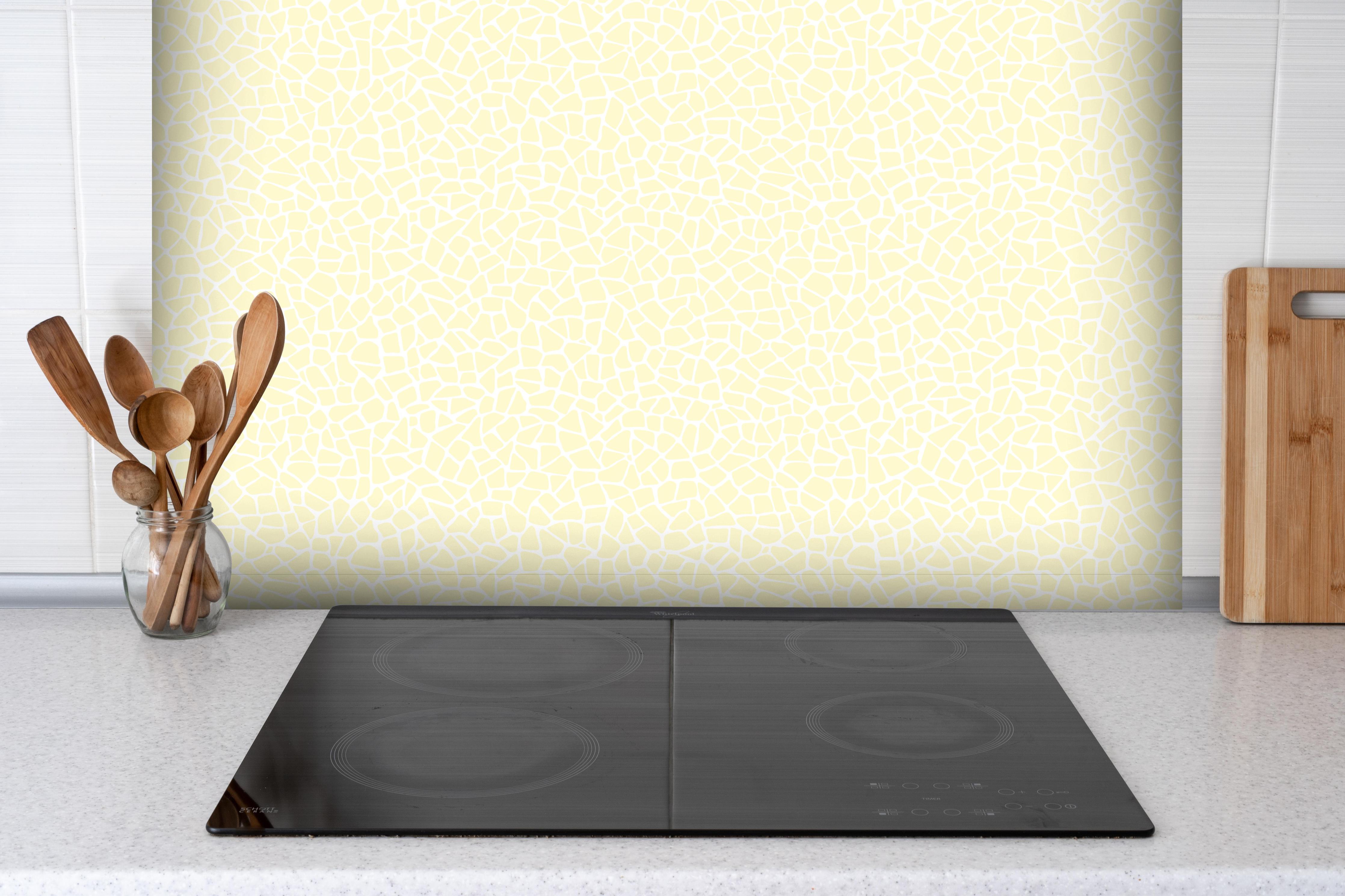 Spritzschutz - Pietre Tessere Limone crema hinter einem Cerankochfeld zwischen Holz-Kochutensilien