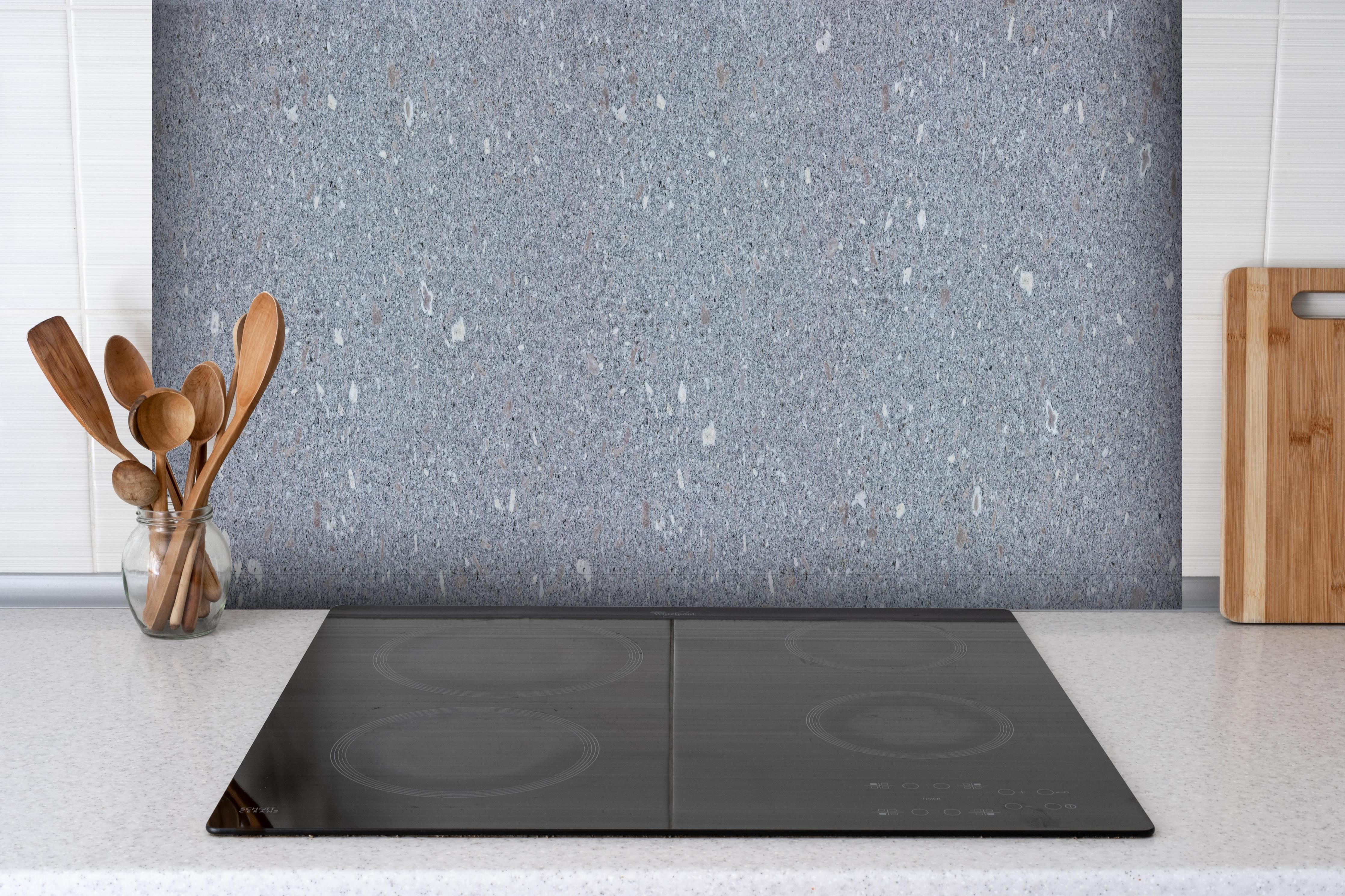 Spritzschutz - Polierter Naturgranit hinter einem Cerankochfeld zwischen Holz-Kochutensilien