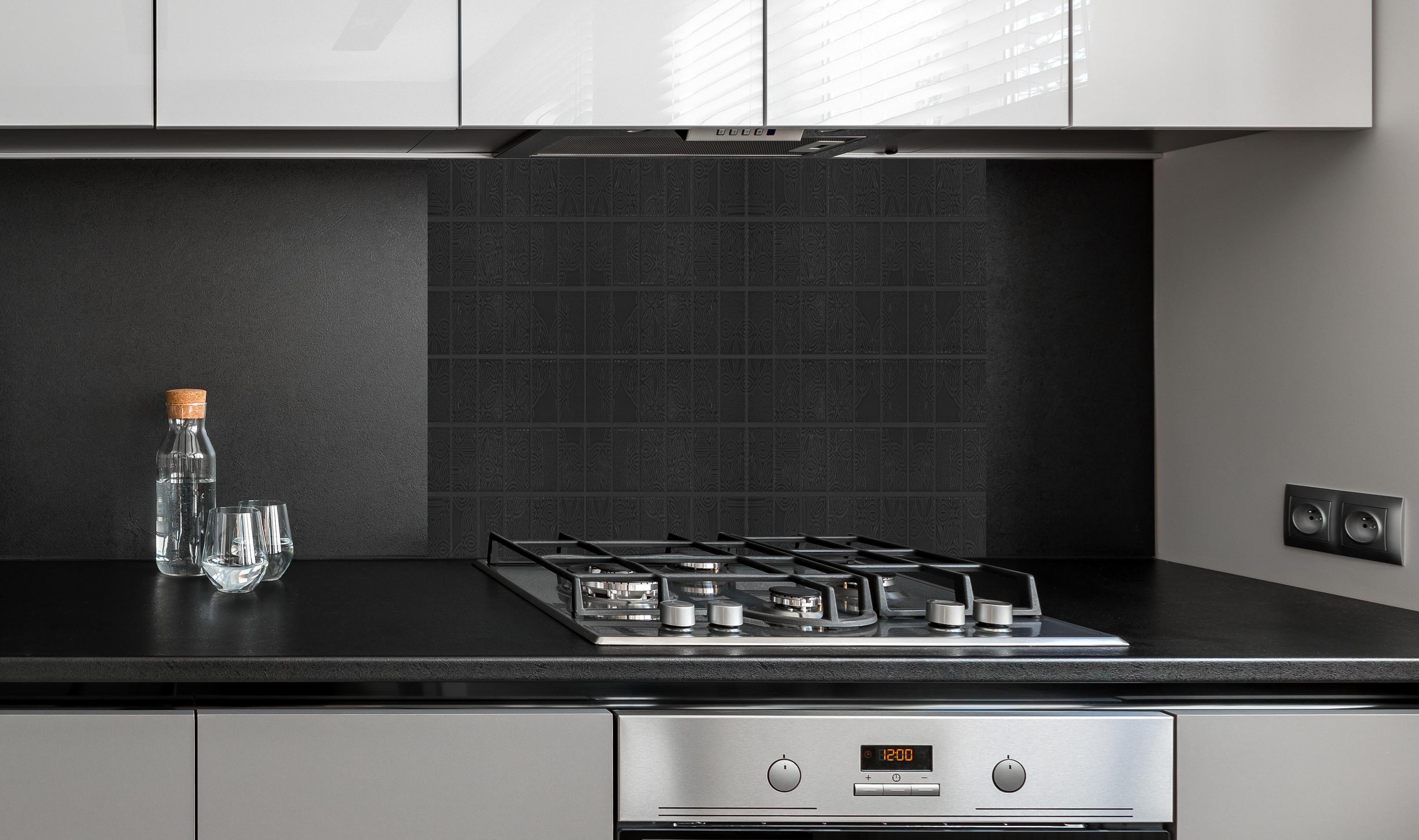 Spritzschutz - Quadratische schwarze Fliesen hinter einem Cerankochfeld zwischen Holz-Kochutensilien