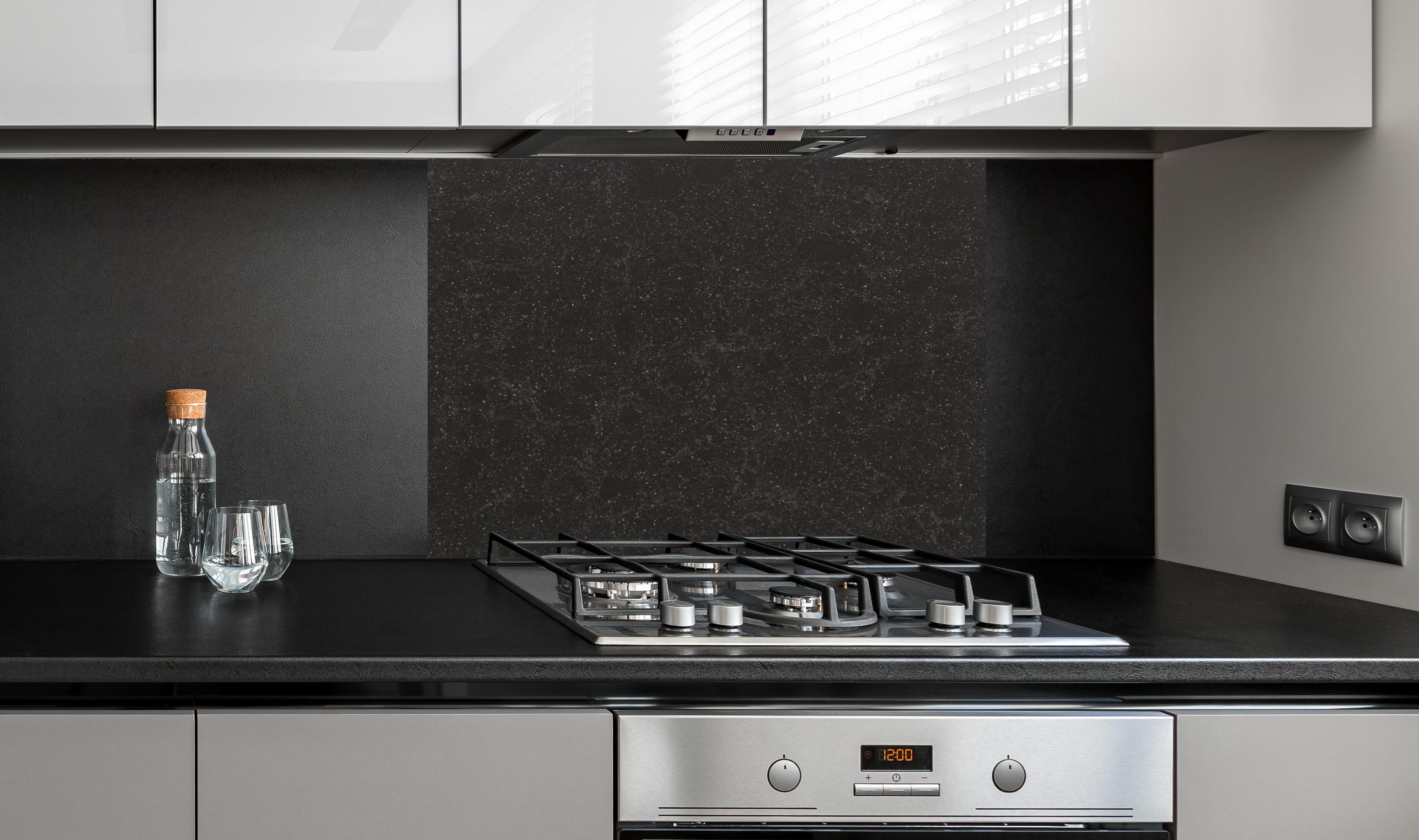 Spritzschutz - Quarz Diamond Black hinter einem Cerankochfeld zwischen Holz-Kochutensilien