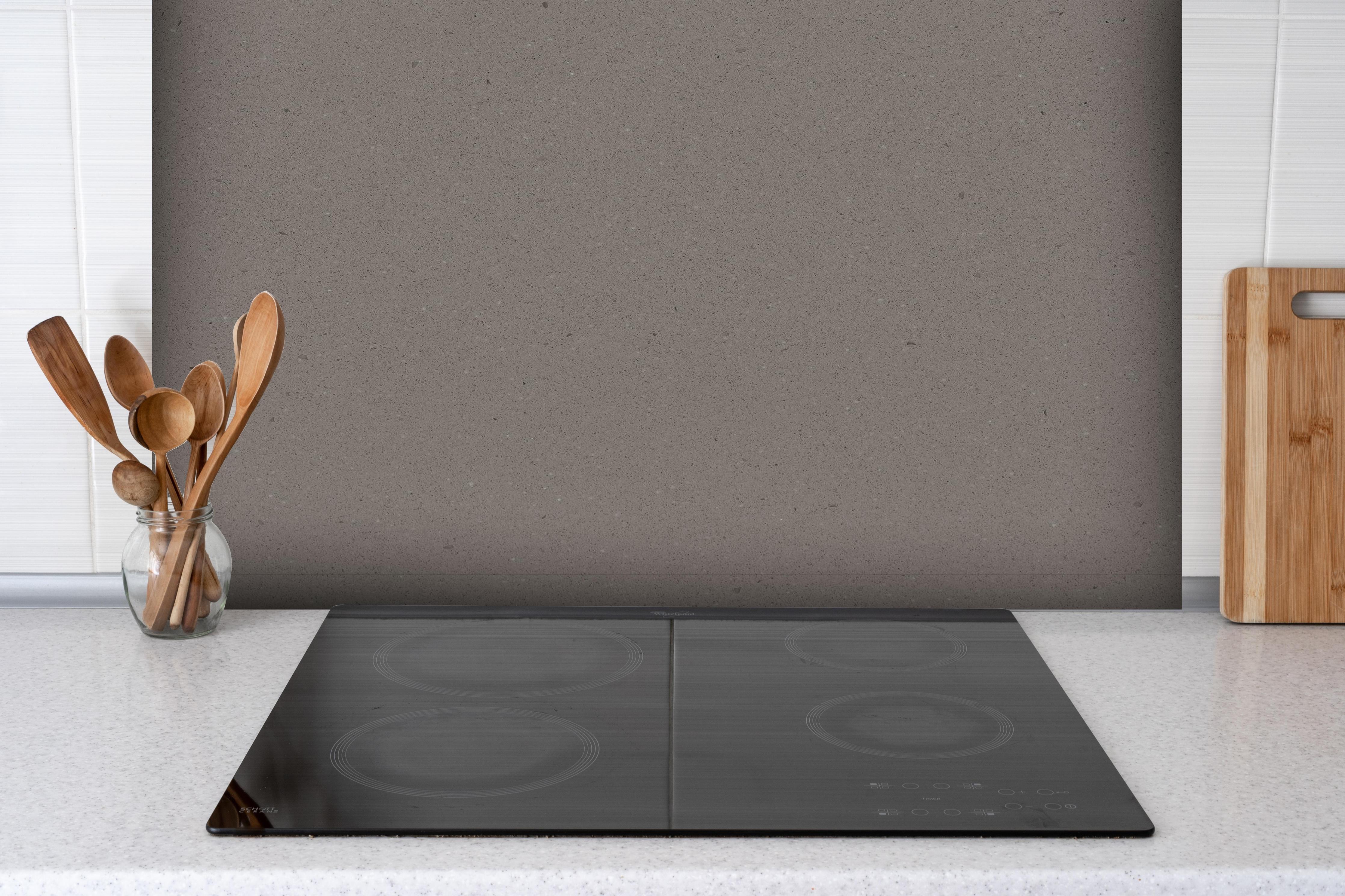 Spritzschutz - Quarz Graphite Grey hinter einem Cerankochfeld zwischen Holz-Kochutensilien