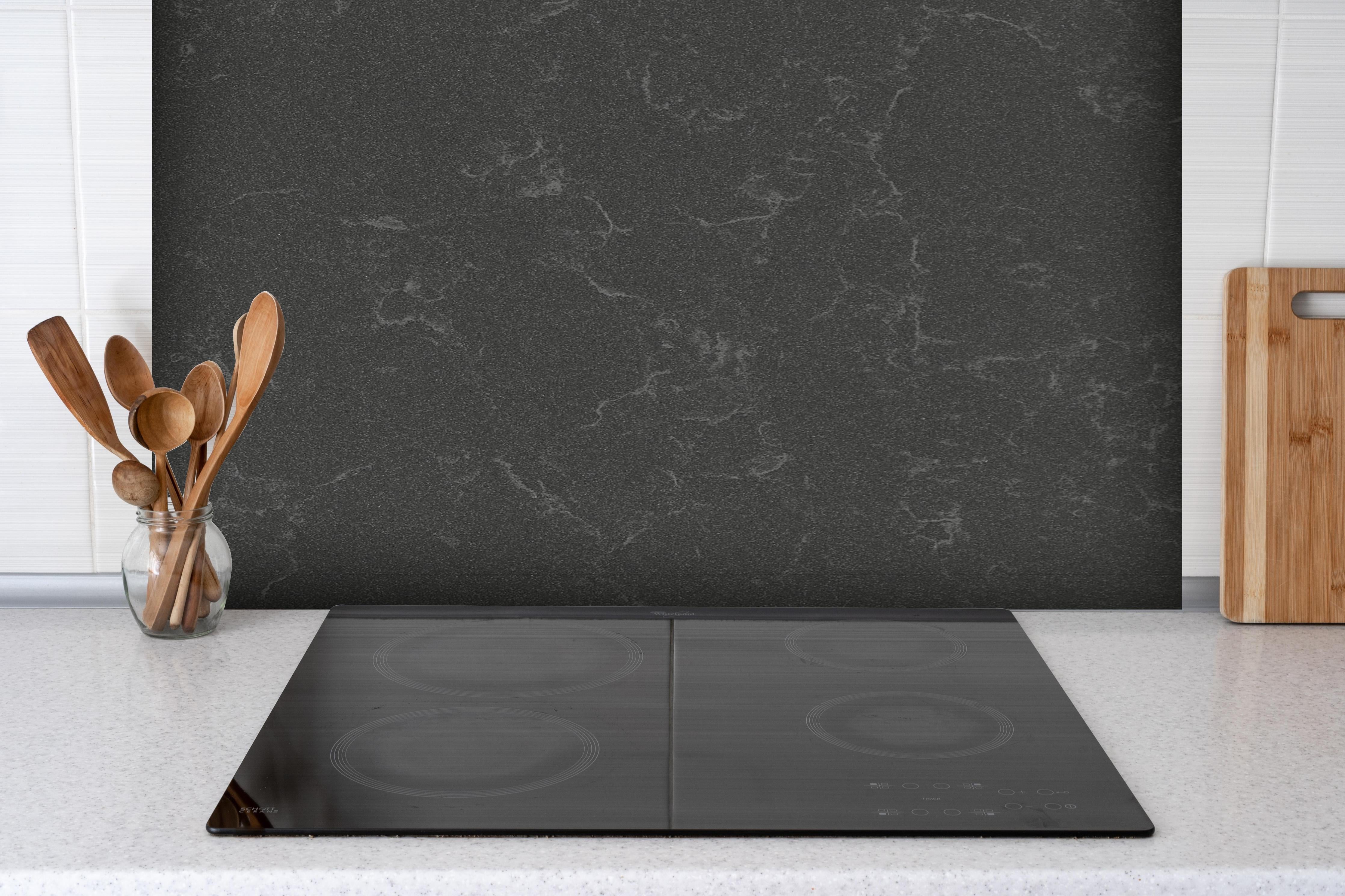 Spritzschutz - Quarz Mineralstone Dark hinter einem Cerankochfeld zwischen Holz-Kochutensilien