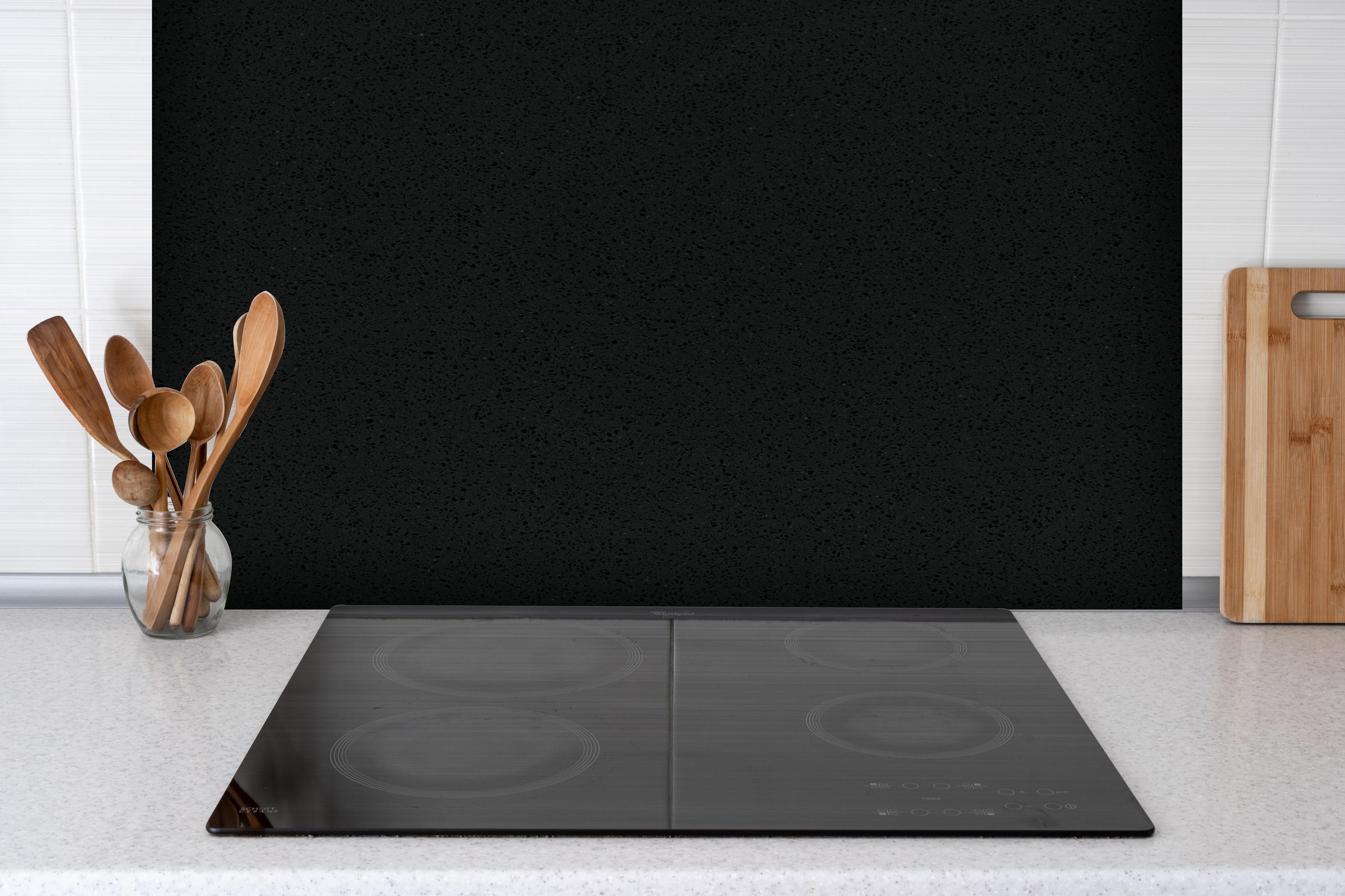 Spritzschutz - Quarz Obsidian Black hinter einem Cerankochfeld zwischen Holz-Kochutensilien
