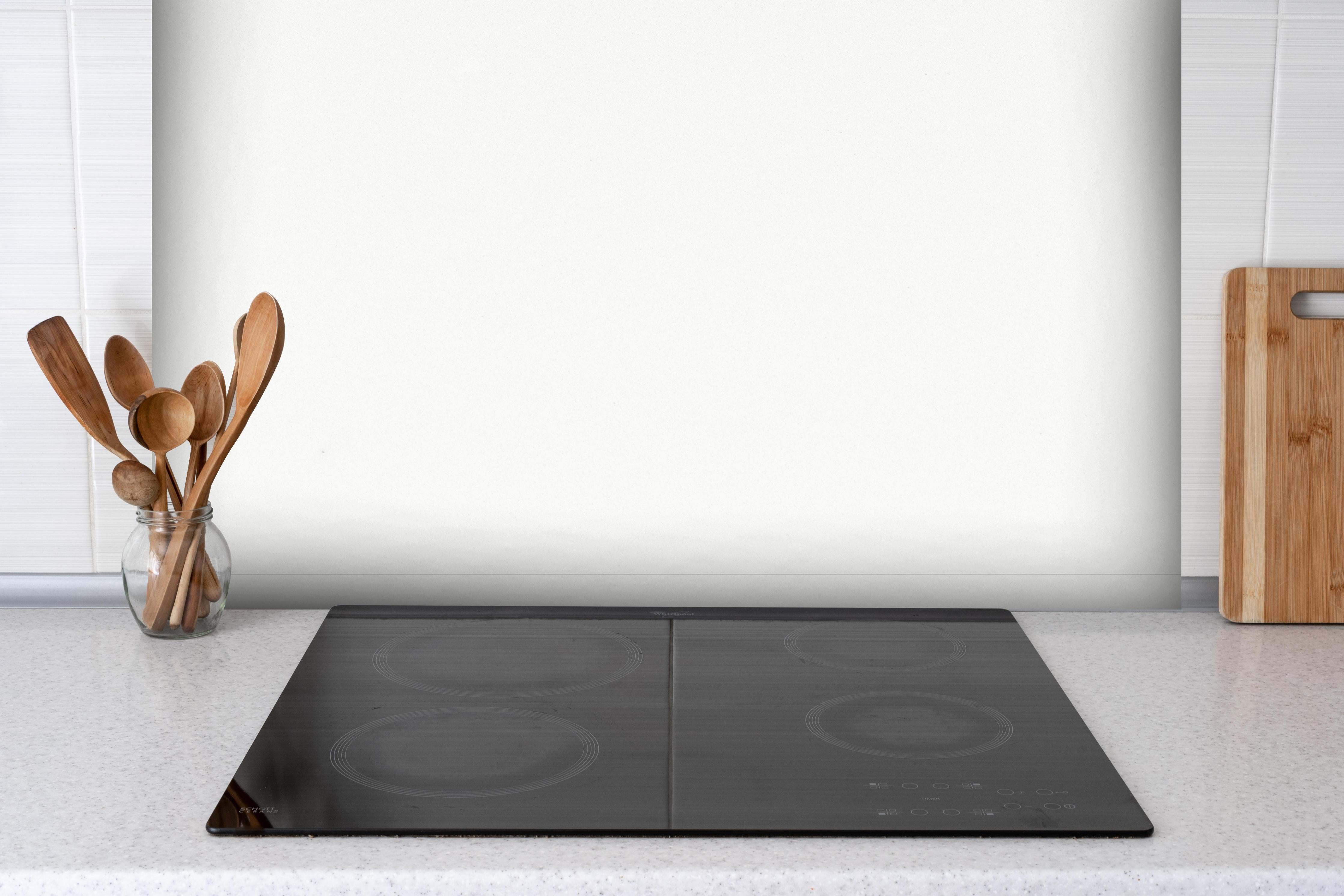 Spritzschutz - Quarz Polar White hinter einem Cerankochfeld zwischen Holz-Kochutensilien