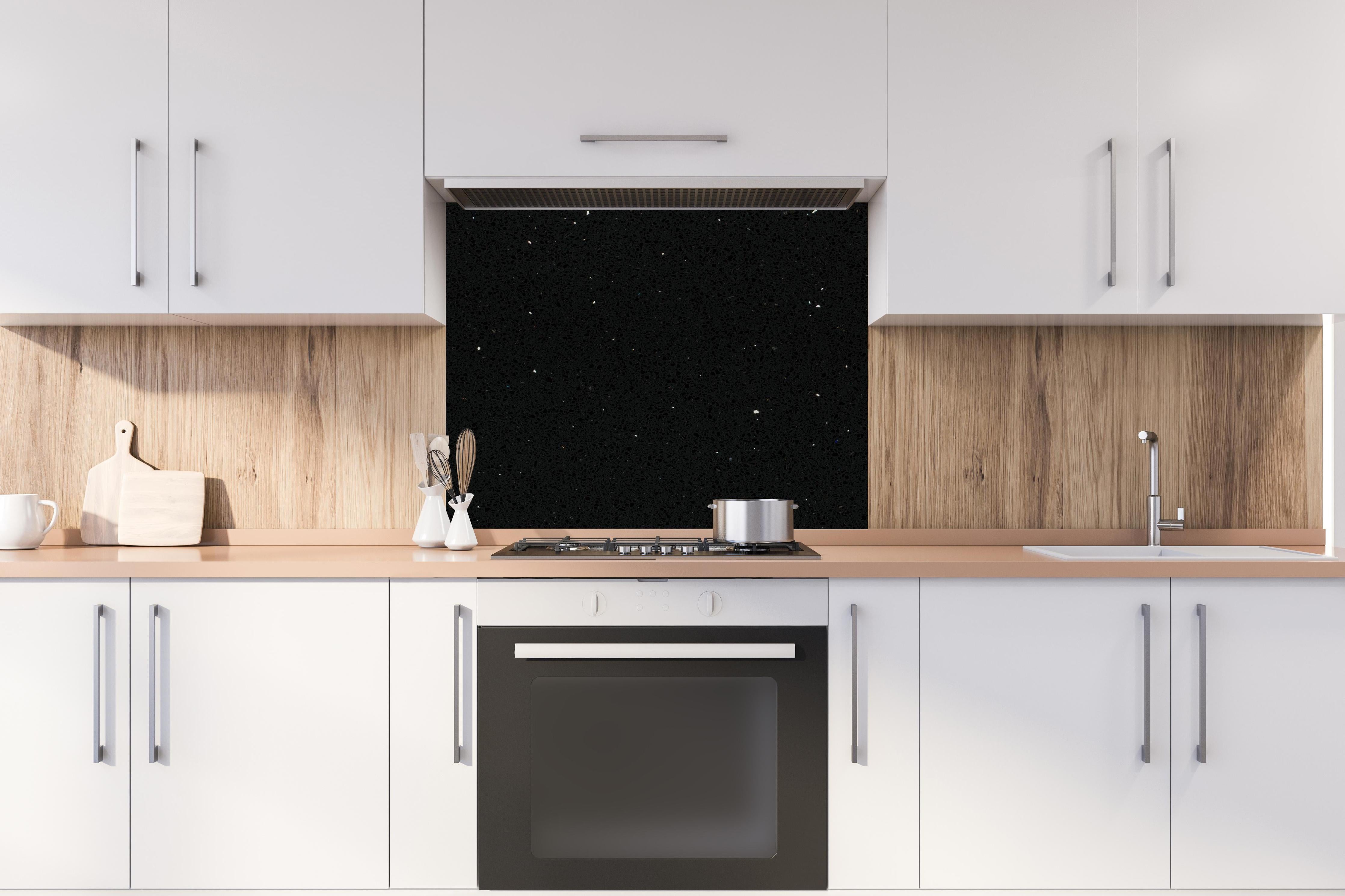 Spritzschutz - Quarz Skydance Black hinter einem Cerankochfeld zwischen Holz-Kochutensilien
