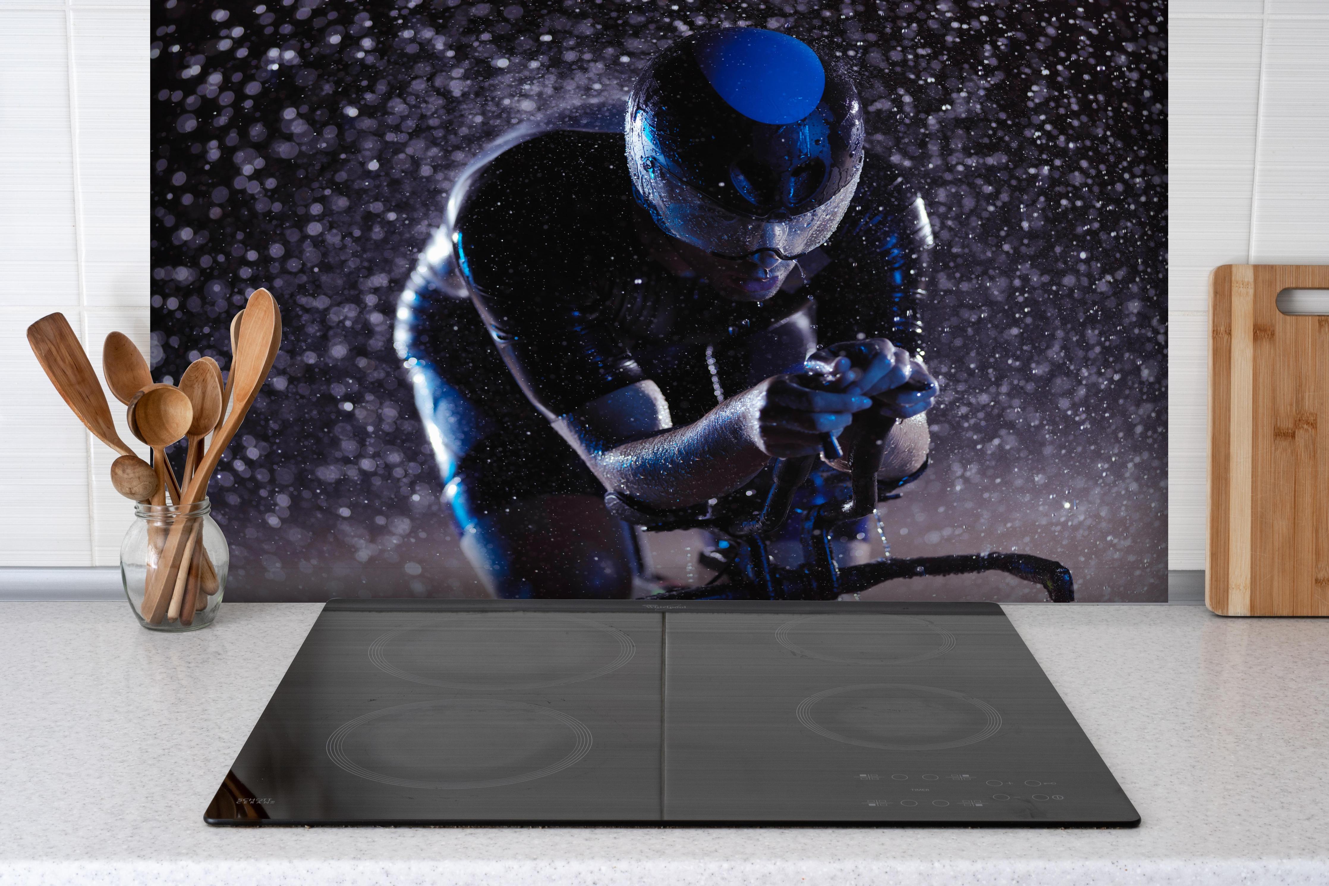 Spritzschutz - Radfahrer nachts bei Regen hinter einem Cerankochfeld zwischen Holz-Kochutensilien