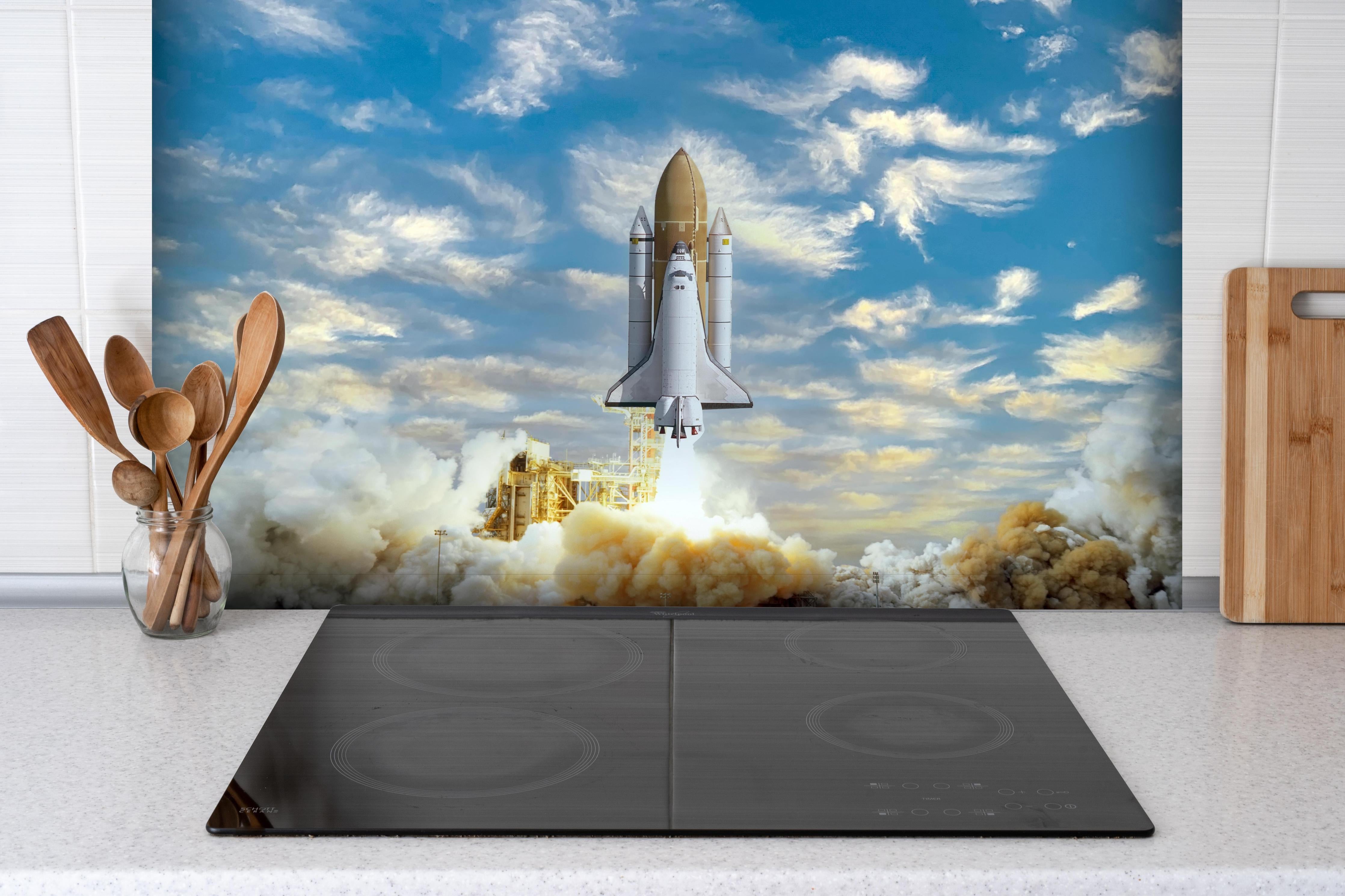 Spritzschutz - Rakete startet ins All hinter einem Cerankochfeld zwischen Holz-Kochutensilien
