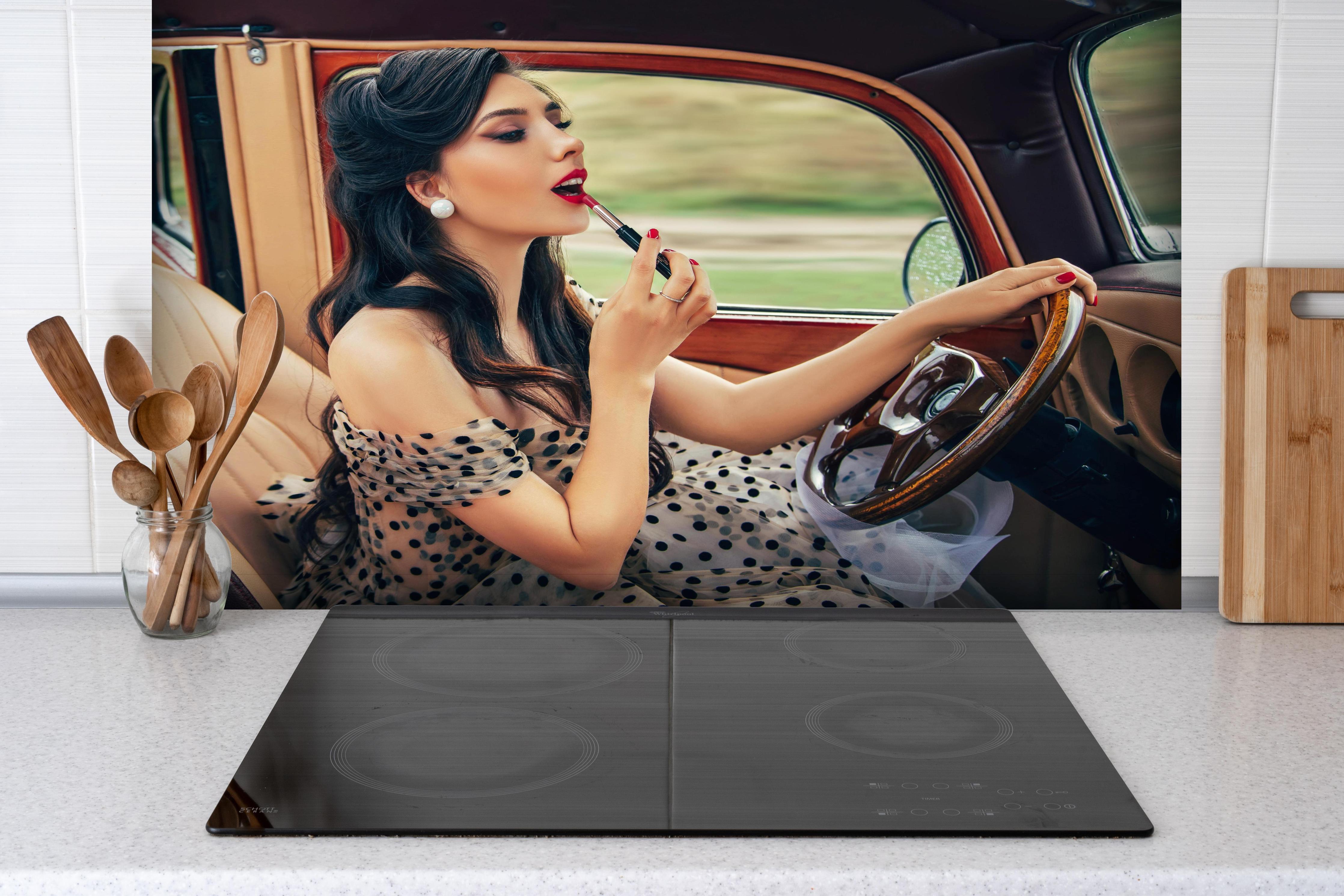 Spritzschutz - Retro Schönheit mit Autolenkrad und Lippenstift hinter einem Cerankochfeld zwischen Holz-Kochutensilien