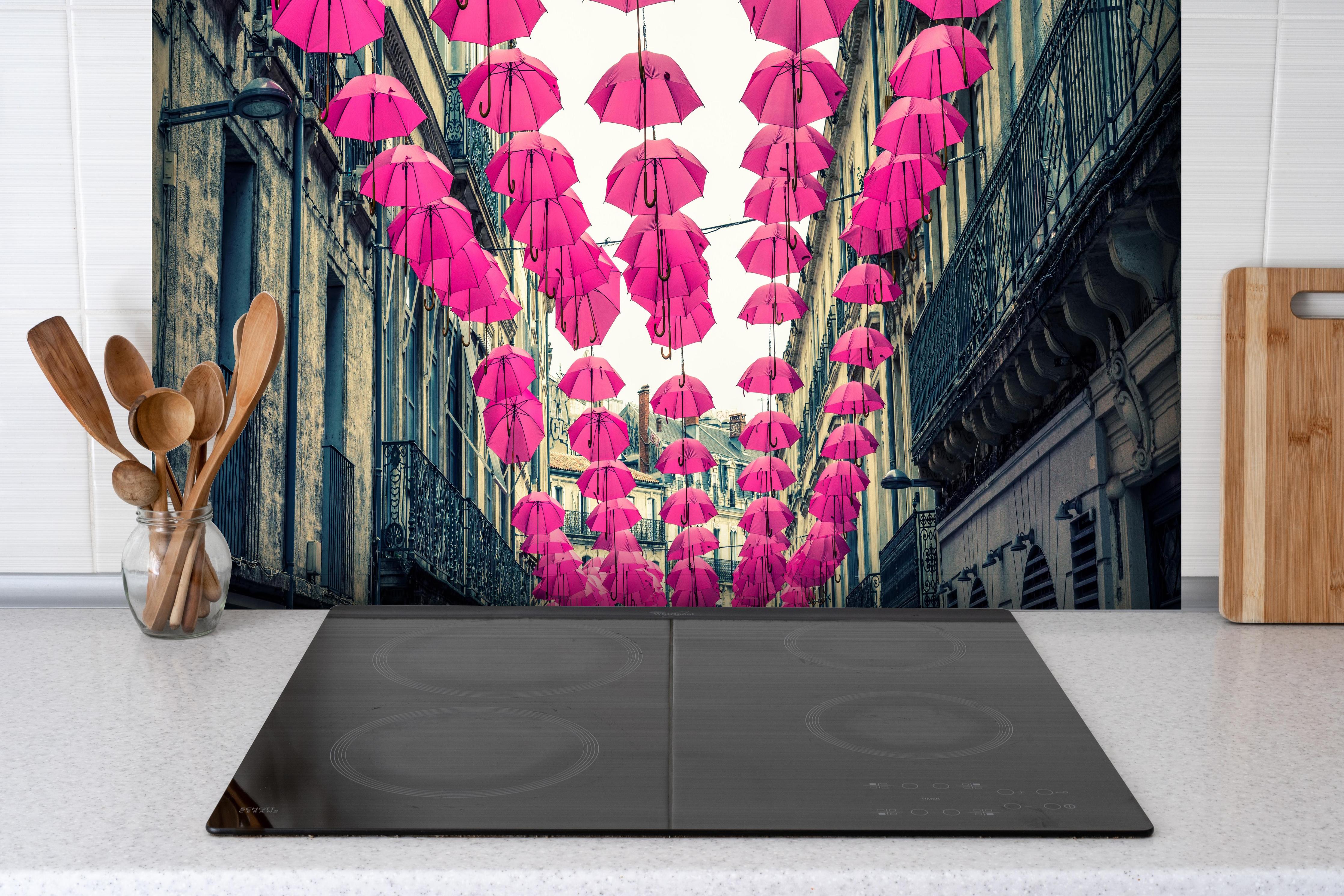 Spritzschutz - Rosafarbene Regenschirme als Straßenkunst hinter einem Cerankochfeld zwischen Holz-Kochutensilien