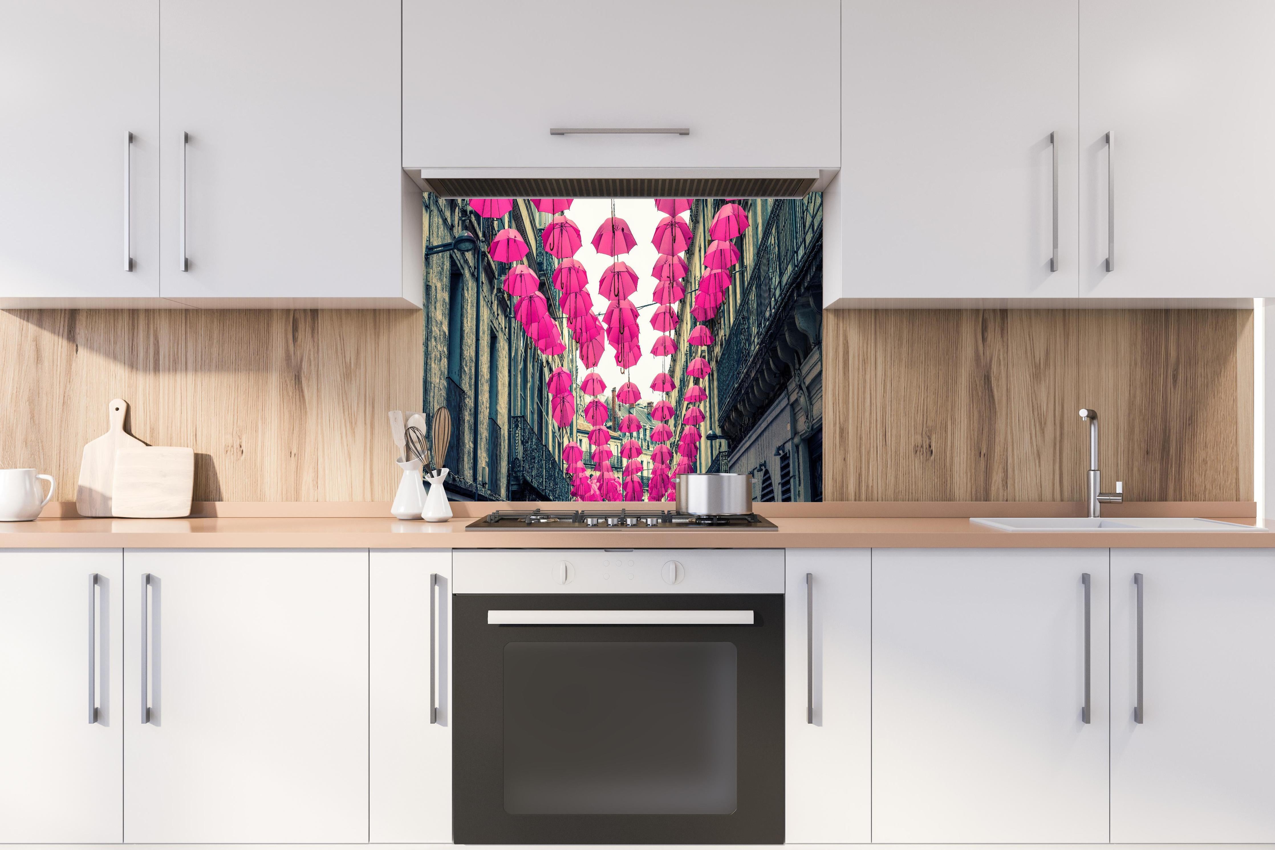 Spritzschutz - Rosafarbene Regenschirme als Straßenkunst hinter einem Cerankochfeld zwischen Holz-Kochutensilien