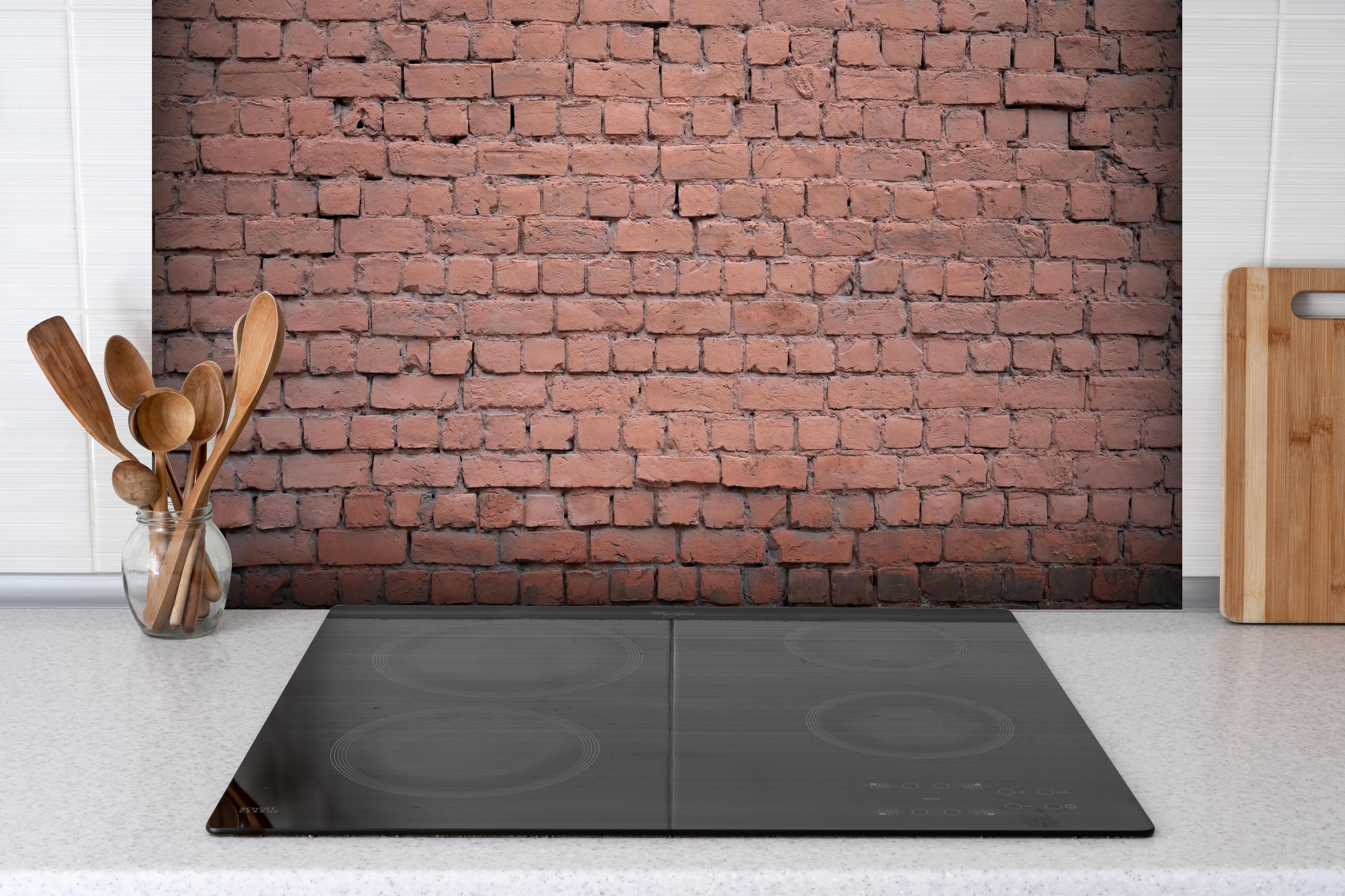 Spritzschutz - Rosafarbige Ziegelwandoberfläche hinter einem Cerankochfeld zwischen Holz-Kochutensilien