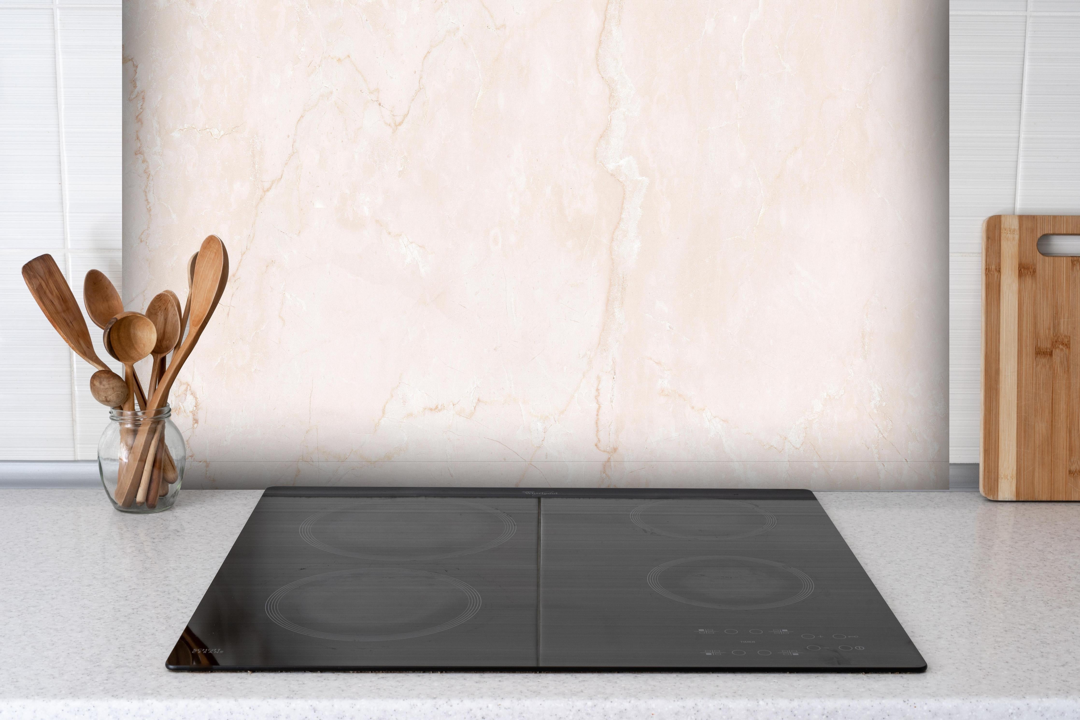 Spritzschutz - Rosafarbige moderne Marmortextur hinter einem Cerankochfeld zwischen Holz-Kochutensilien